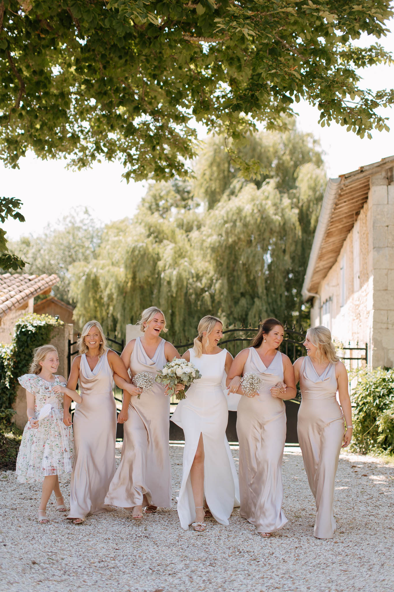 Bride and four bridesmaids in champagne satin with flower girl walking on gravel path