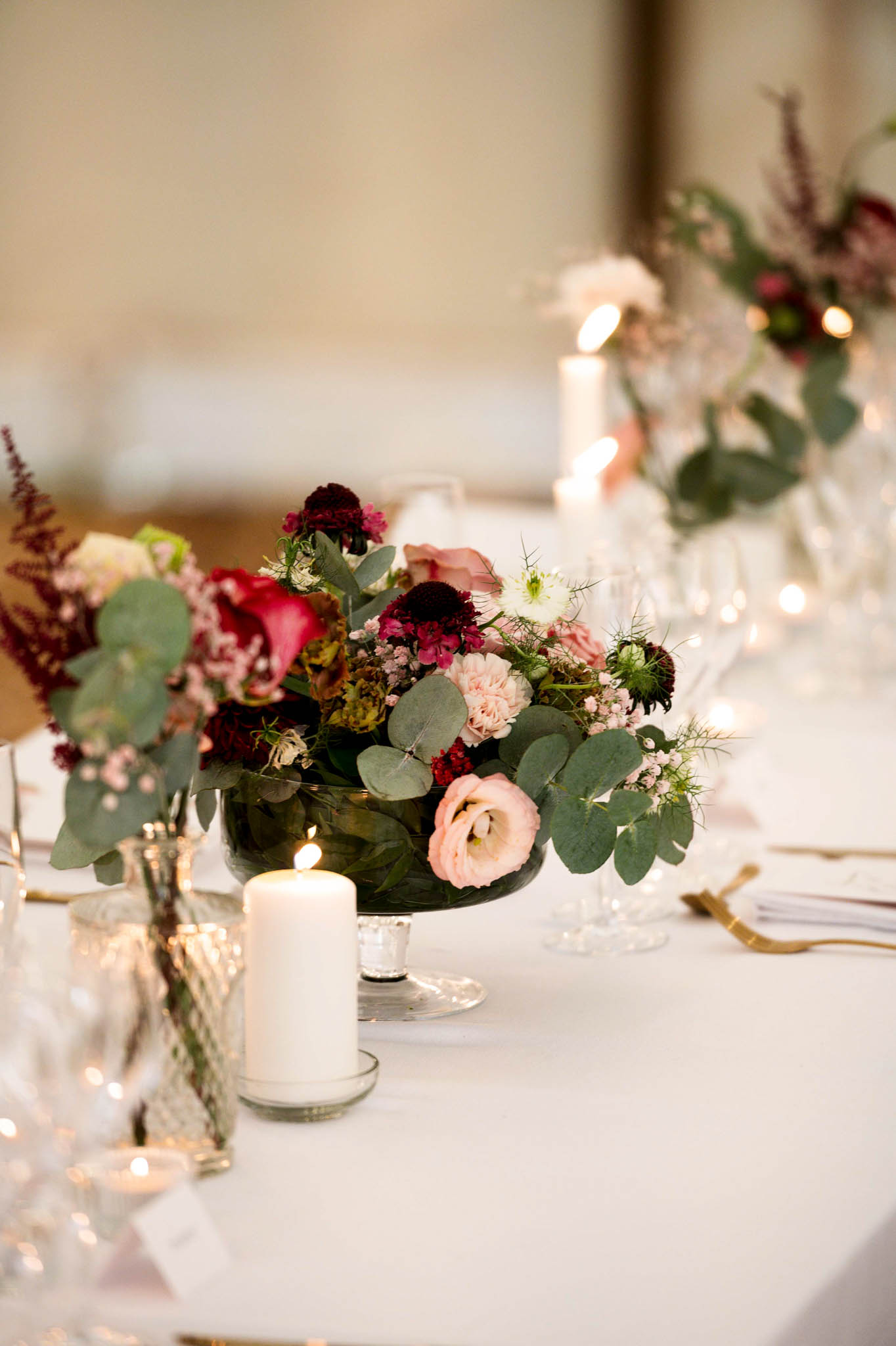Reception table centerpiece with burgundy scabiosa blush lisianthus and ranunculus with candlelight