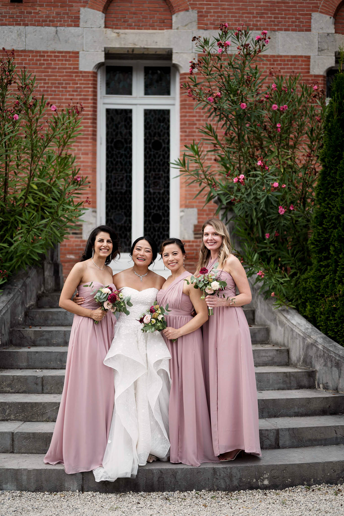 Bride in lace ruffle gown with three bridesmaids in mauve chiffon on chateau entrance steps