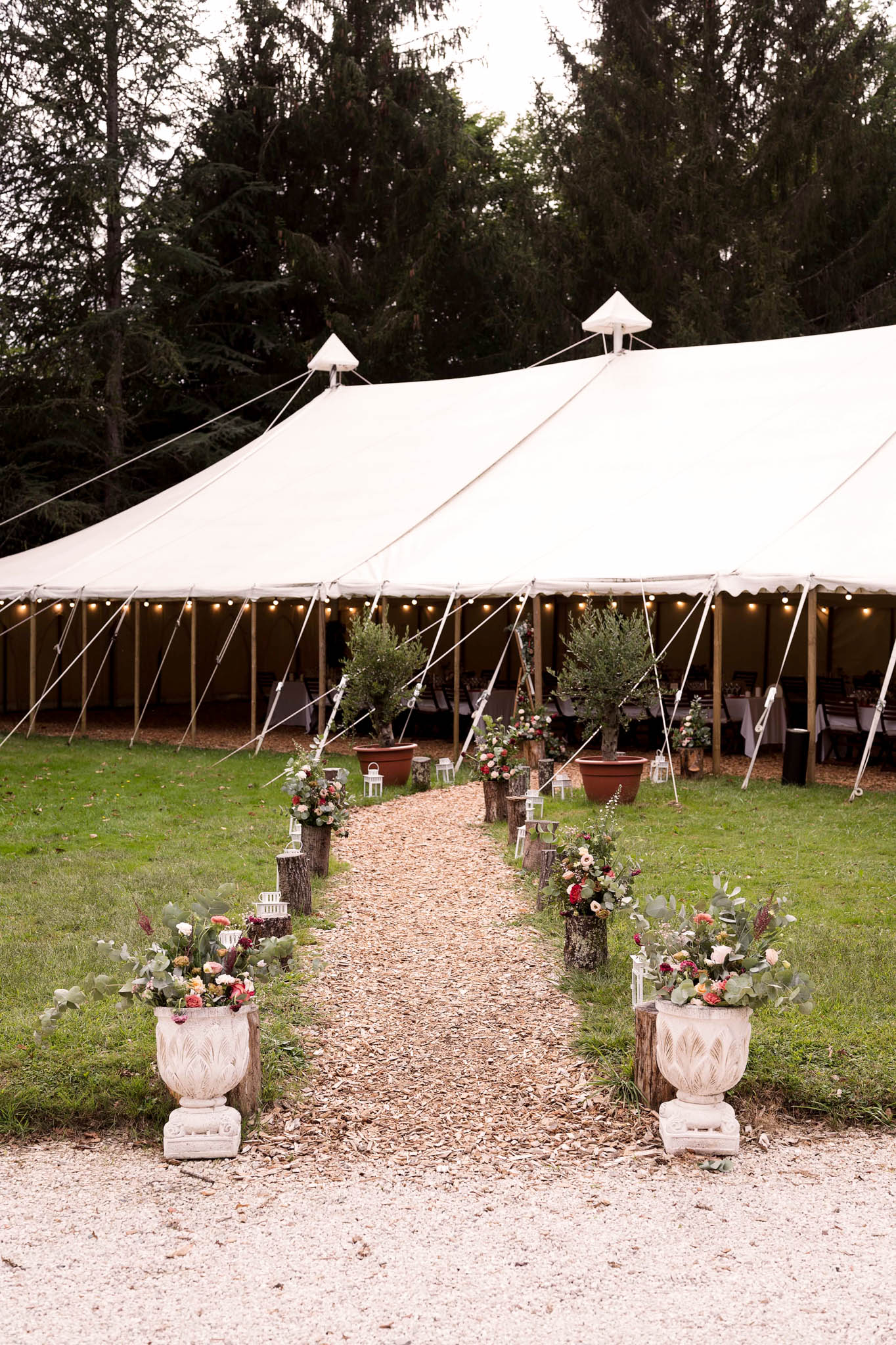 White sailcloth marquee with fairy lights and rustic pathway lined with floral urns and lanterns at dusk
