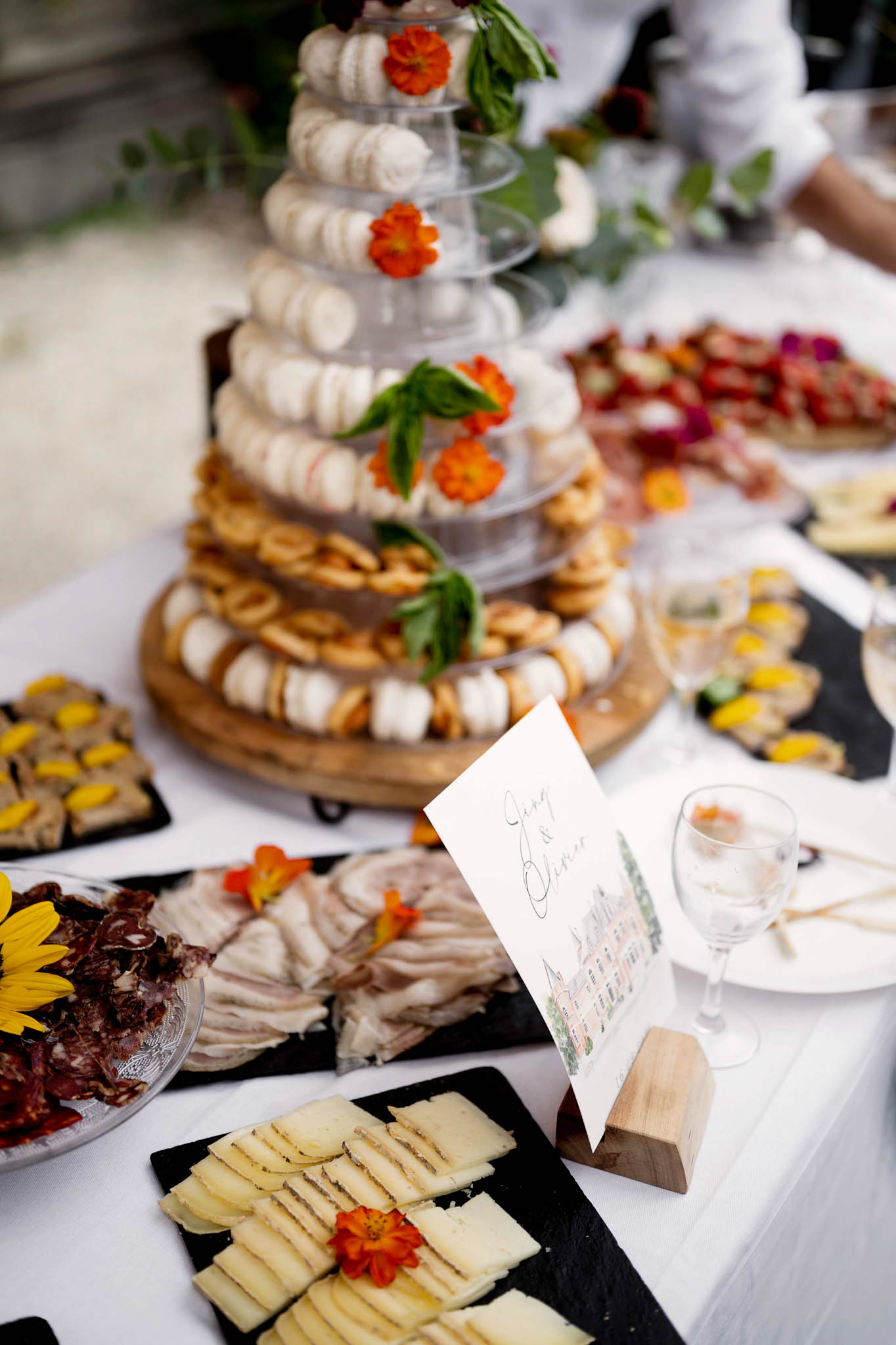Macaron tower with orange flowers alongside charcuterie boards canapes and calligraphy wedding card