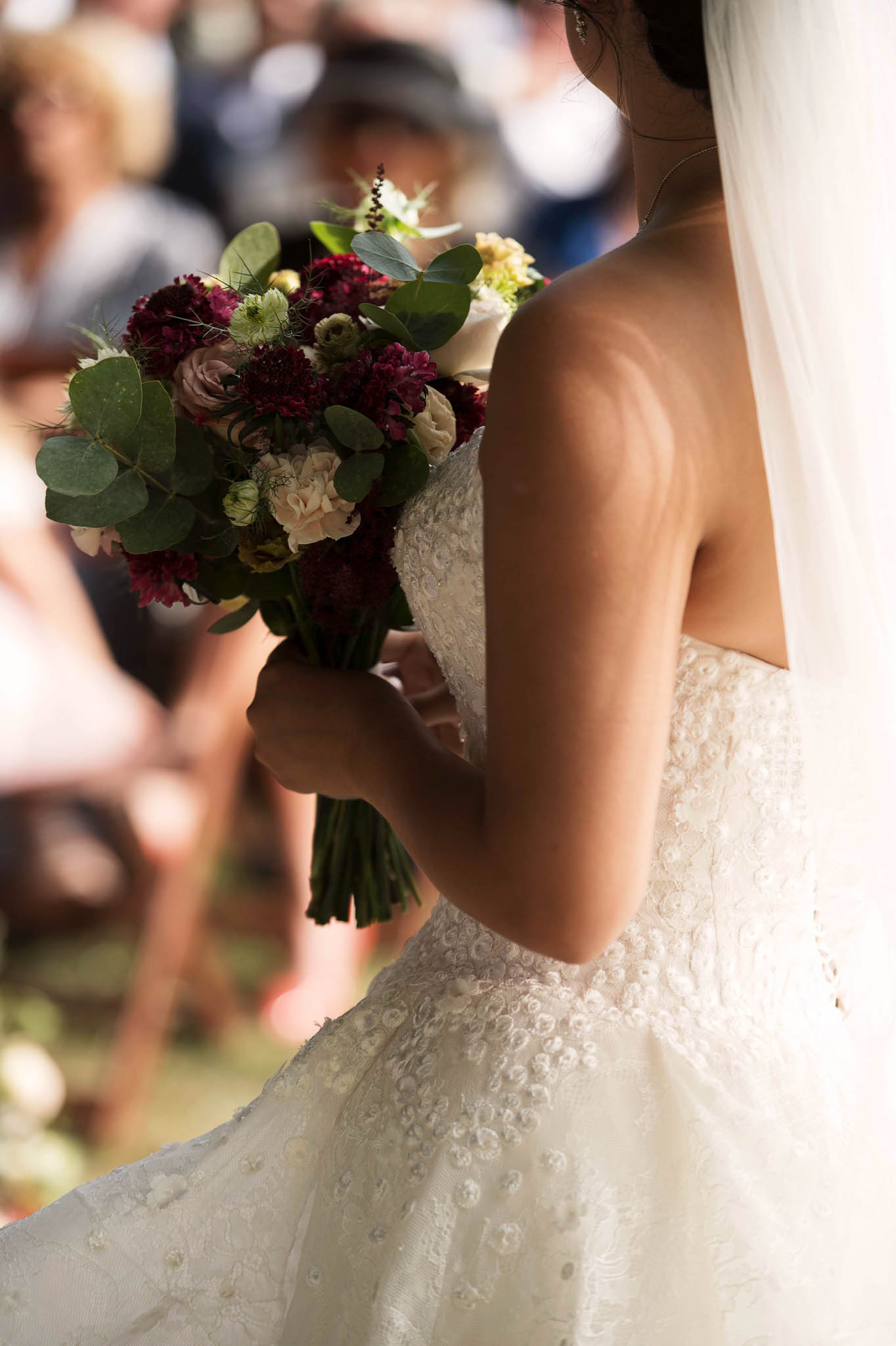 Close-up of bride holding bouquet of burgundy scabiosa, mauve roses, and cream lisianthus with lace bodice detail