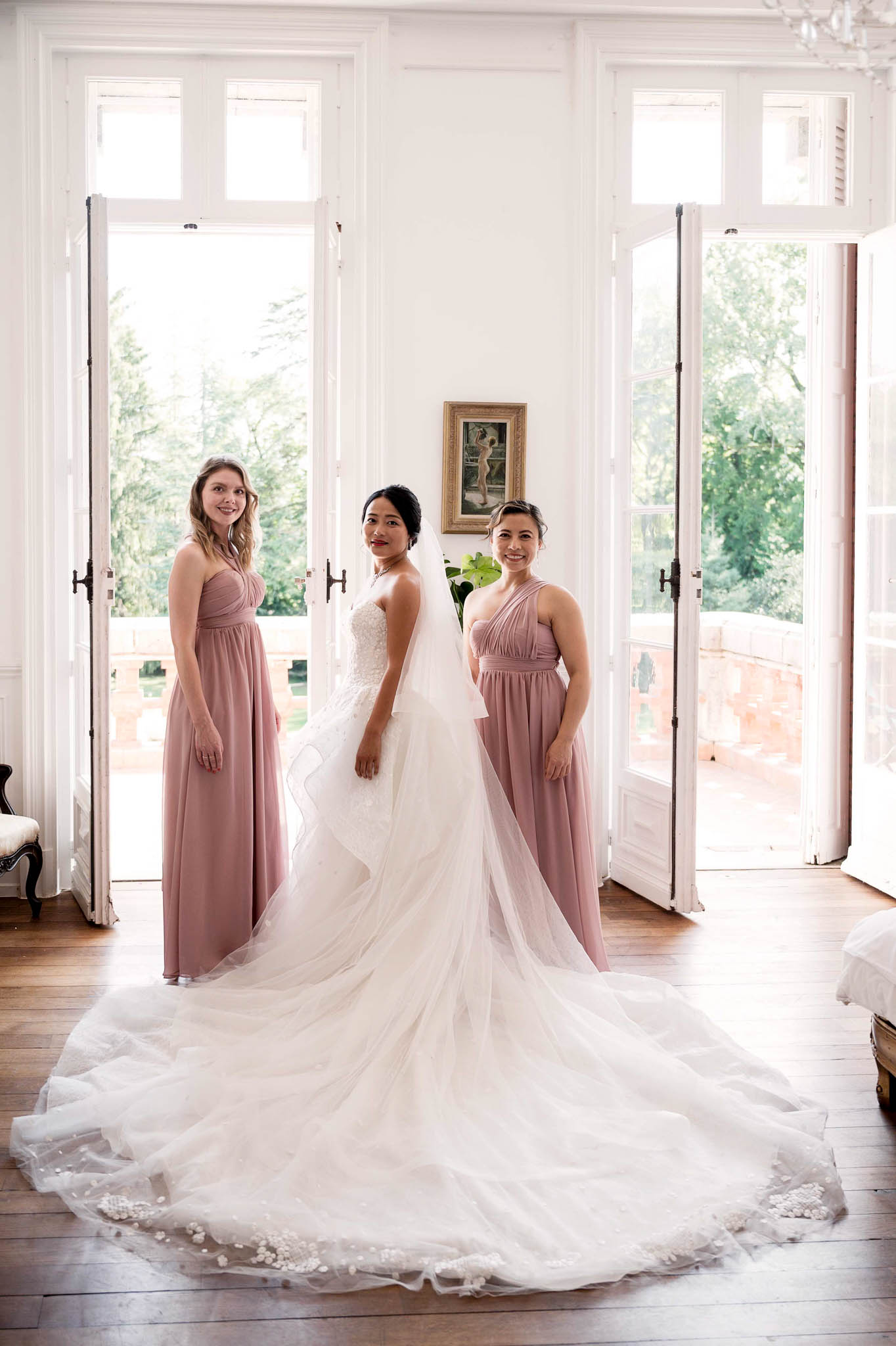Bride in strapless lace ball gown with cathedral train flanked by two bridesmaids in dusty rose dresses