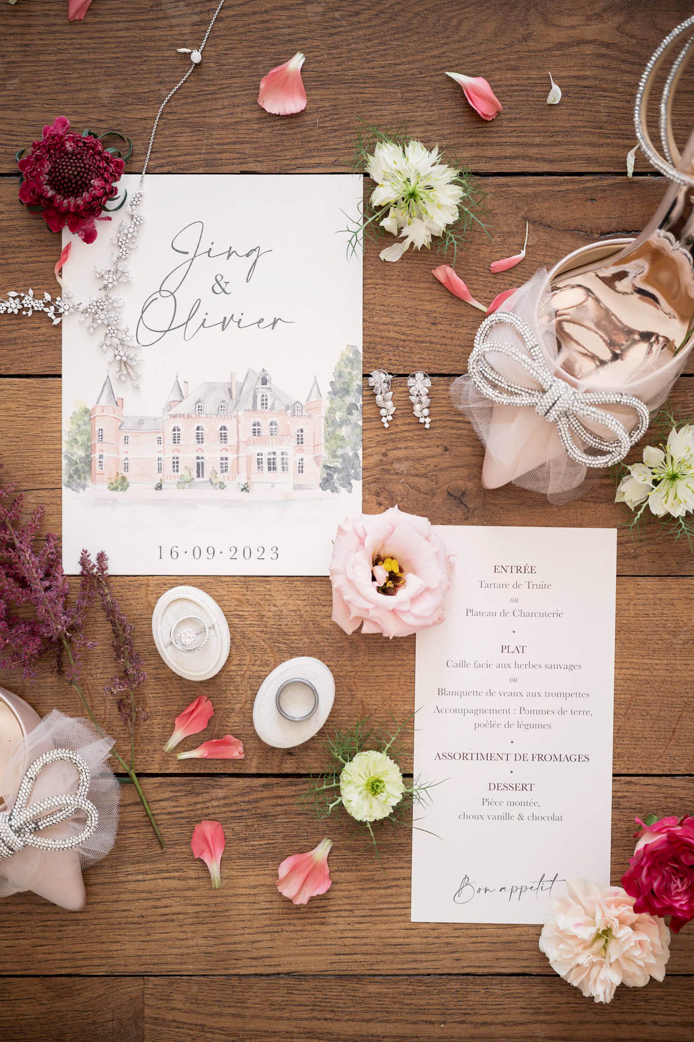 Watercolor chateau invitation with blush satin heels, diamond earrings, and scattered burgundy scabiosa blooms