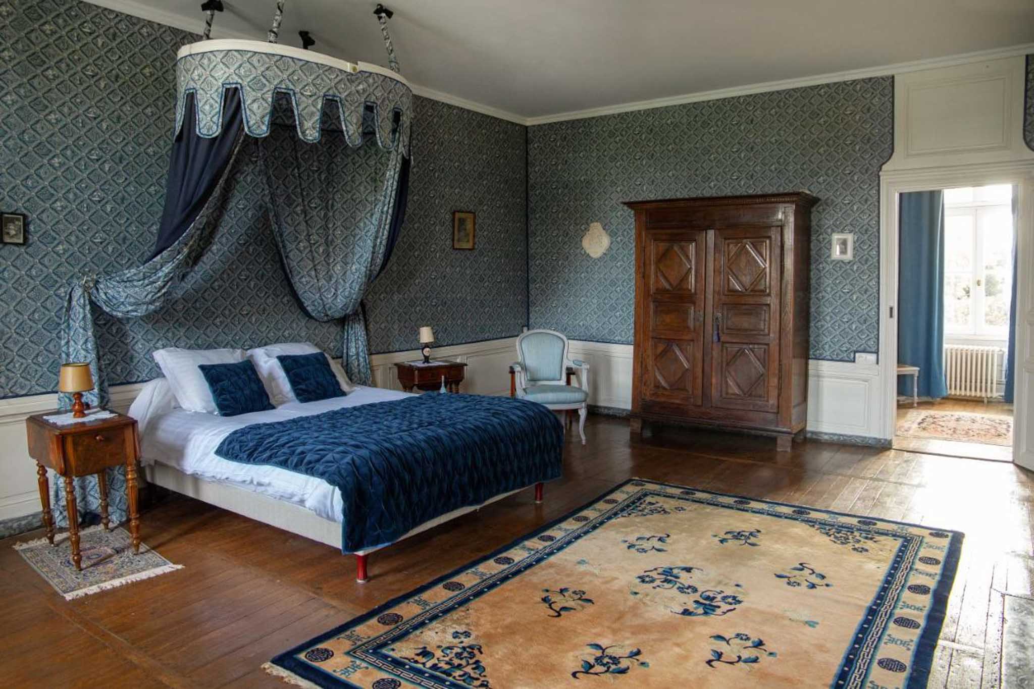 Blue-grey diamond-wallpapered chateau bedroom with navy canopy bed, walnut armoire, and Chinese rug