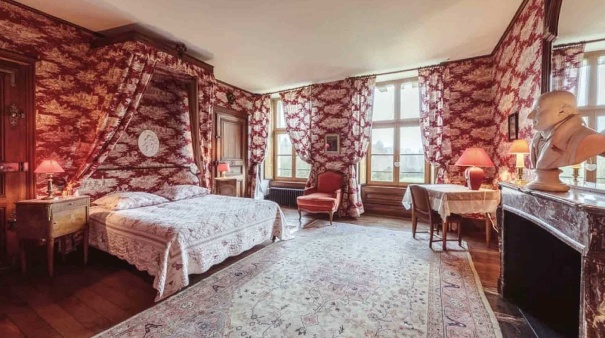 Chateau bedroom suite with crimson toile de Jouy wallpaper four-poster canopy bed and marble fireplace
