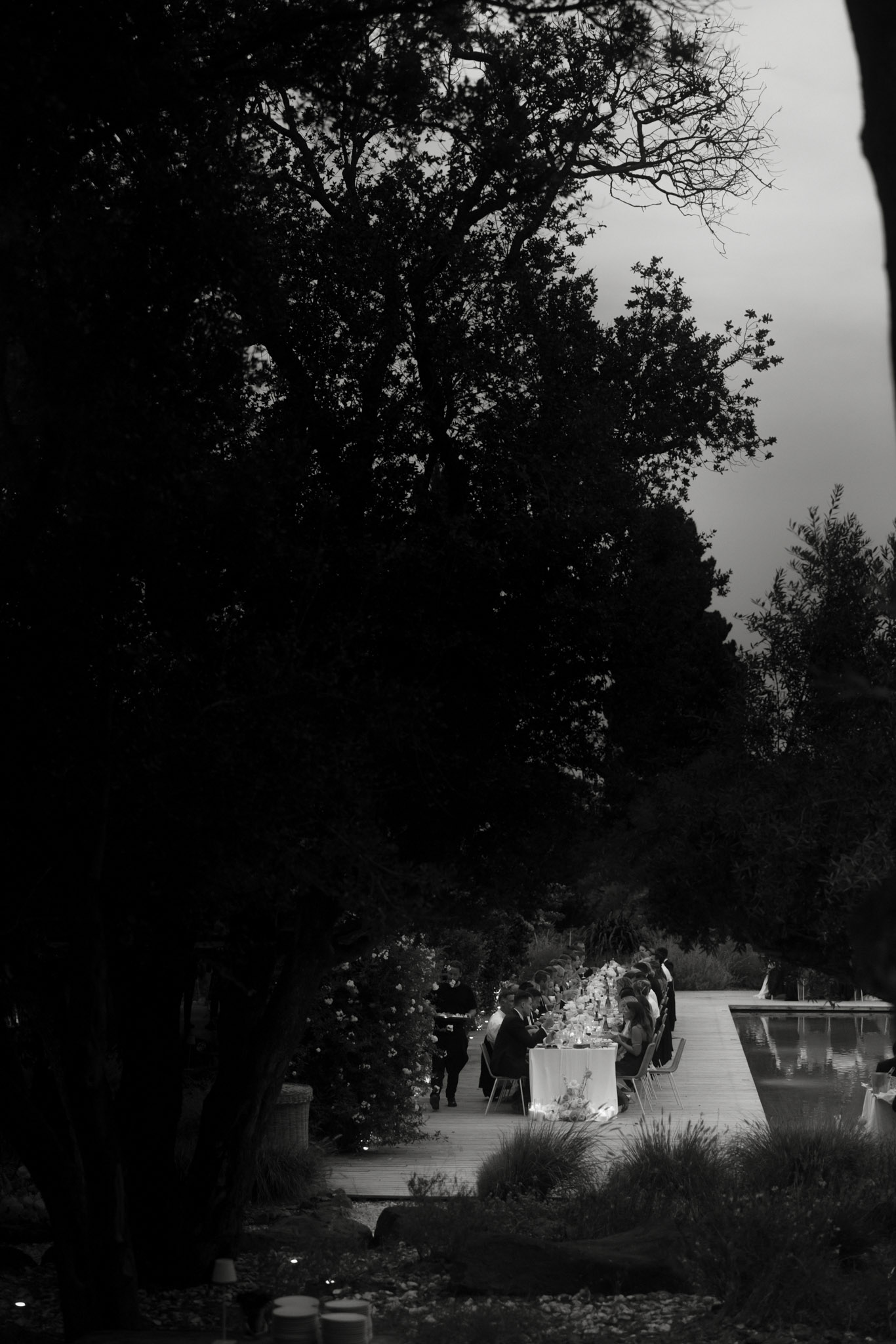 Black and white aerial view of candlelit reception dinner table beside reflecting pool at night
