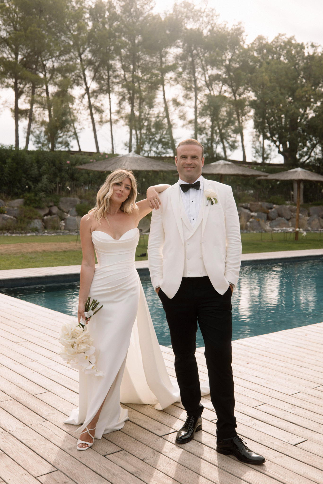 Couple on pool deck, bride in ivory ruched gown with calla lily bouquet, groom in ivory dinner jacket