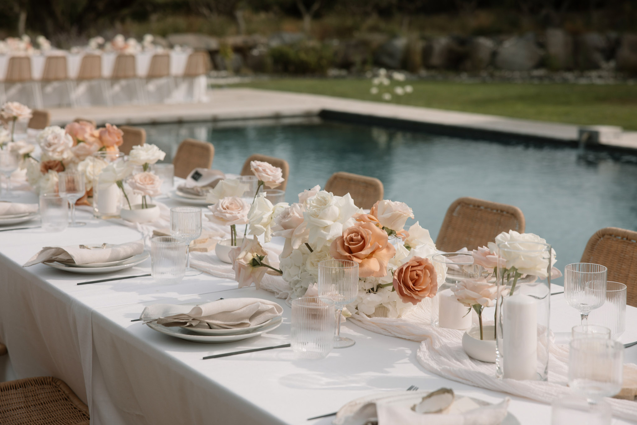 Poolside table with ivory hydrangea and peach rose centerpieces bud vases pillar candles and rattan chairs