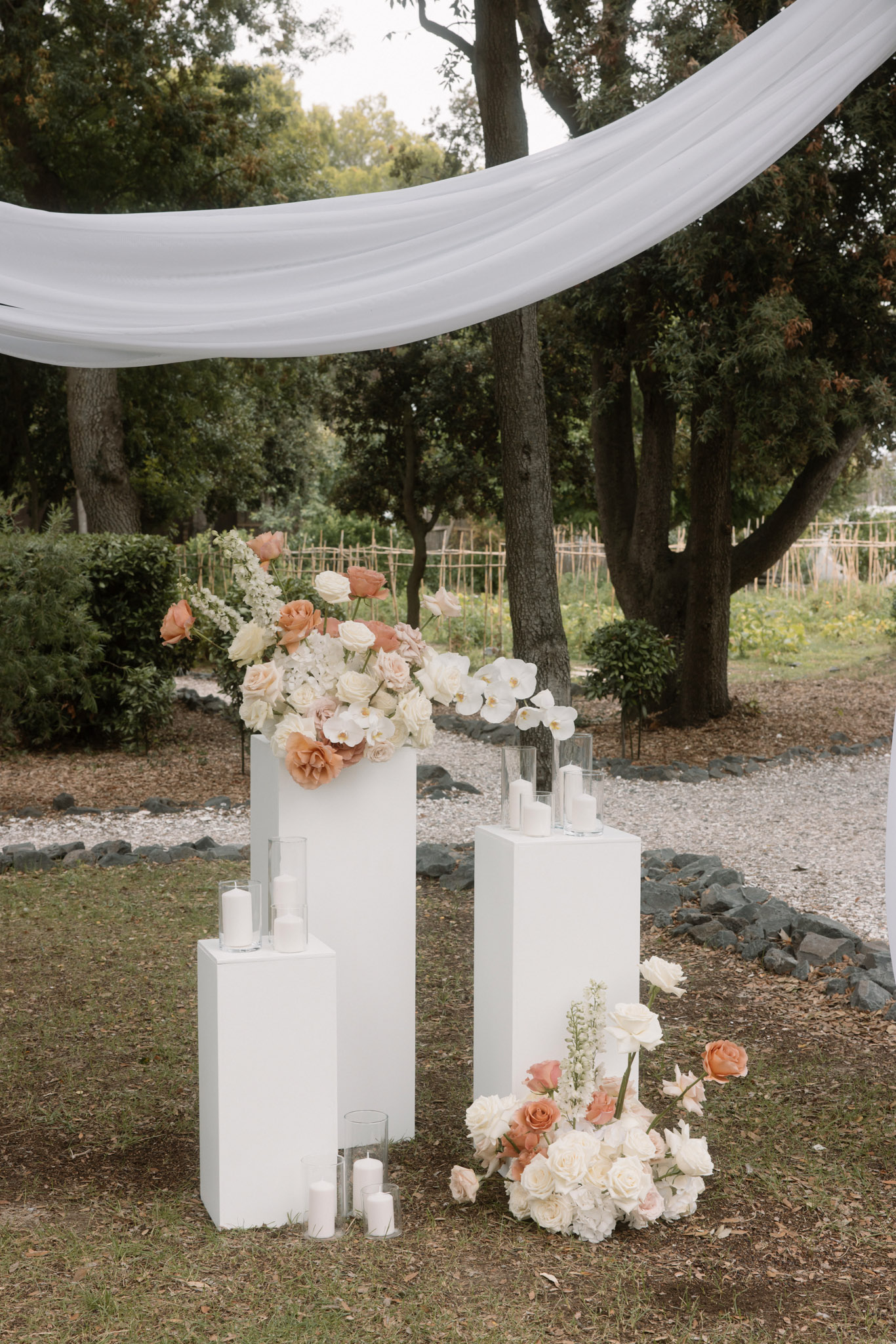 Ceremony altar with white geometric plinths topped with terracotta and blush roses, orchids, and sheer fabric draping