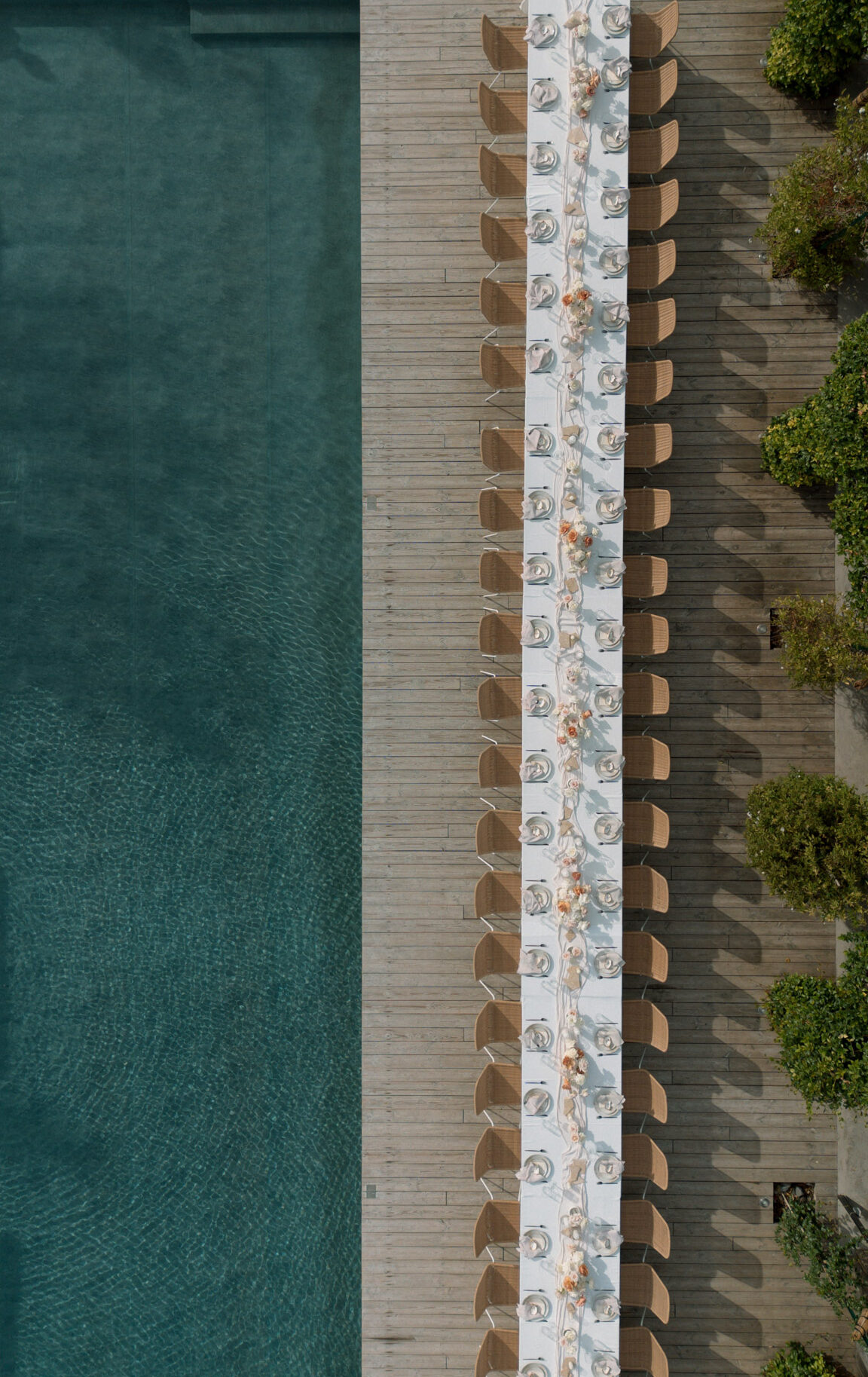 Aerial view of long poolside reception table with rattan chairs and peach floral centerpieces