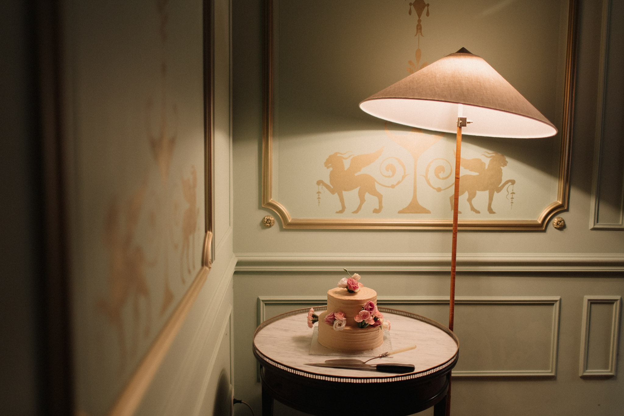 Two-tier semi-naked wedding cake with pink roses and white ranunculus in a sage green panelled chateau room