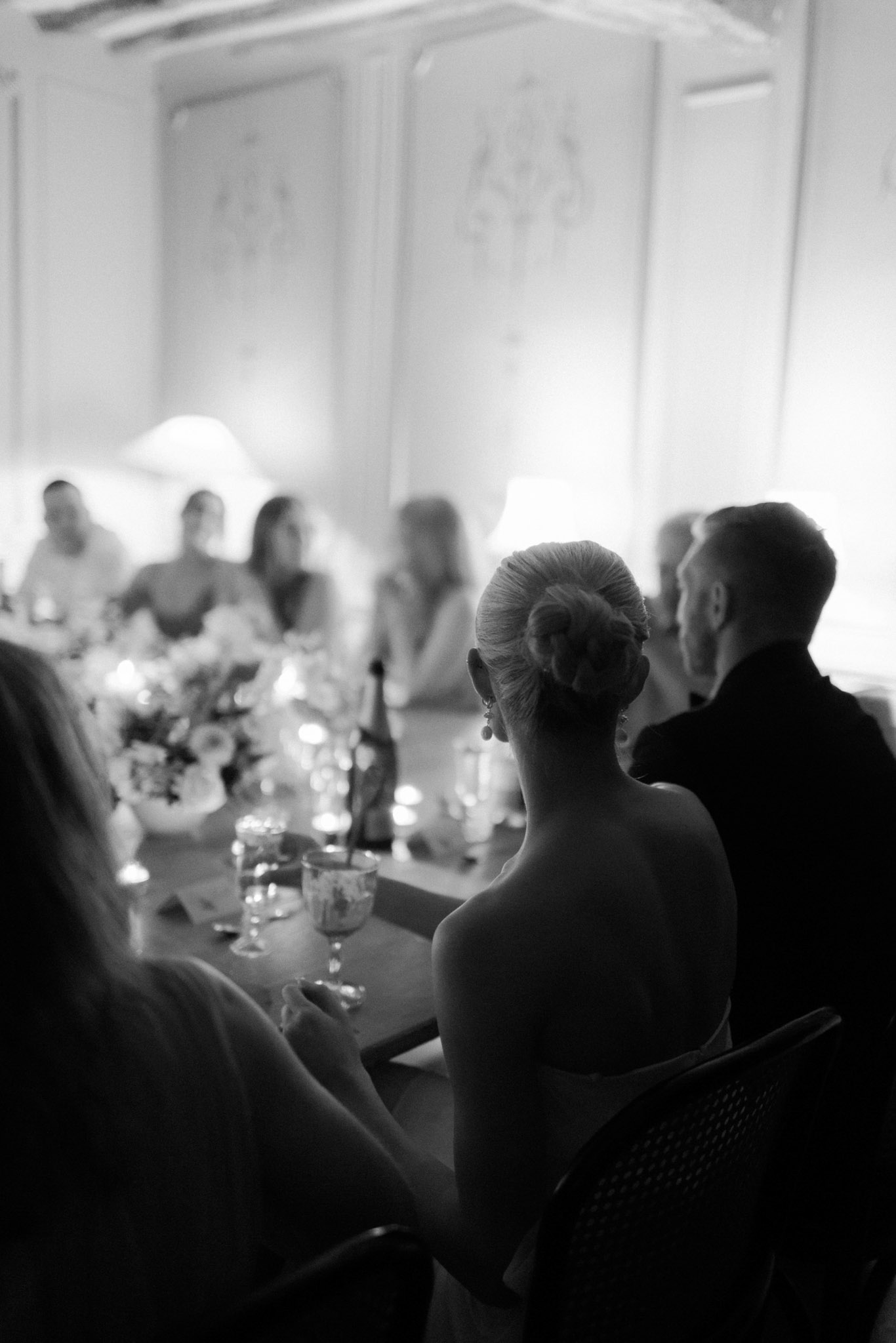 Black and white reception speech with couple from behind, candlelit table and panelled walls with moulding