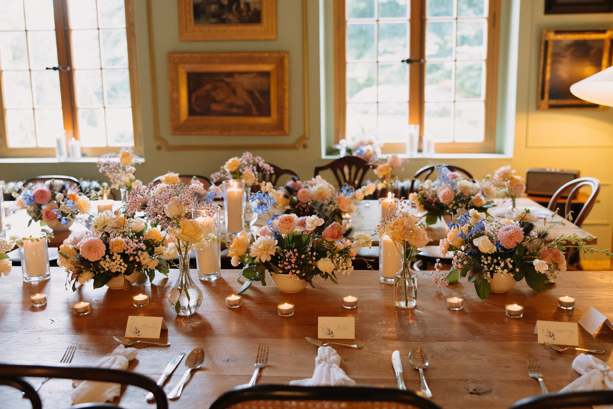 Farm table with blush dahlia, blue delphinium, and peach rose centrepieces in country house dining room
