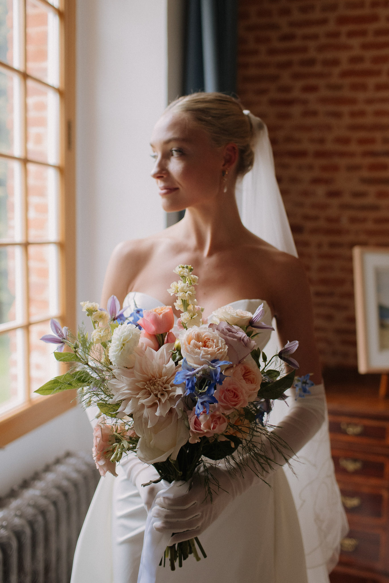 Bride in ivory gown with elbow gloves holding garden bouquet of blush dahlias and blue delphinium