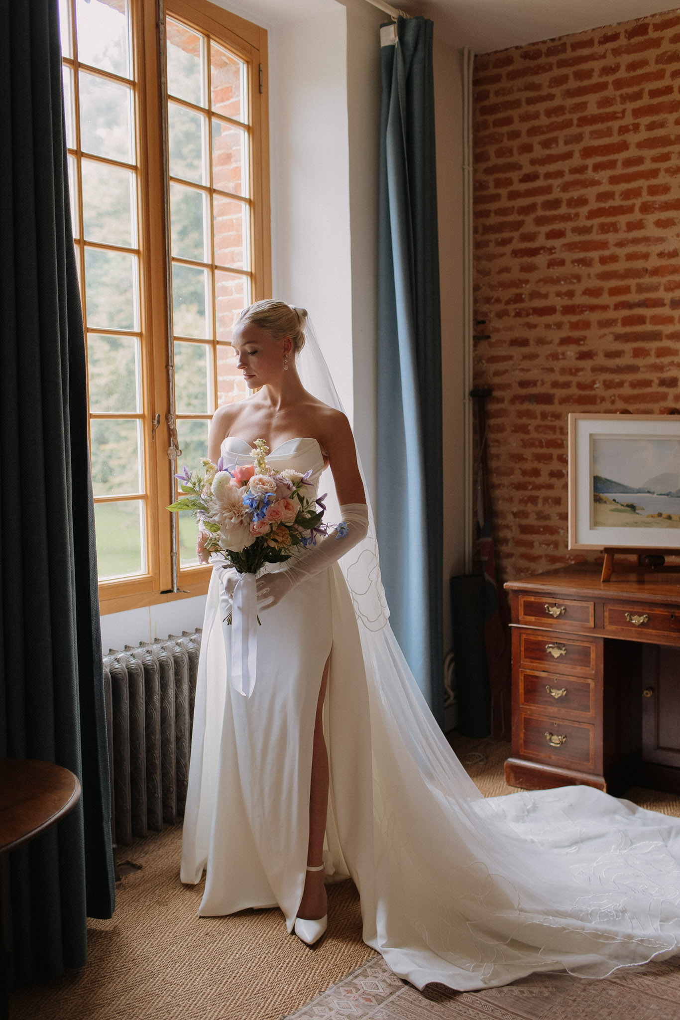 Bride in ivory column gown with gloves and lace veil holding blush rose and blue delphinium bouquet