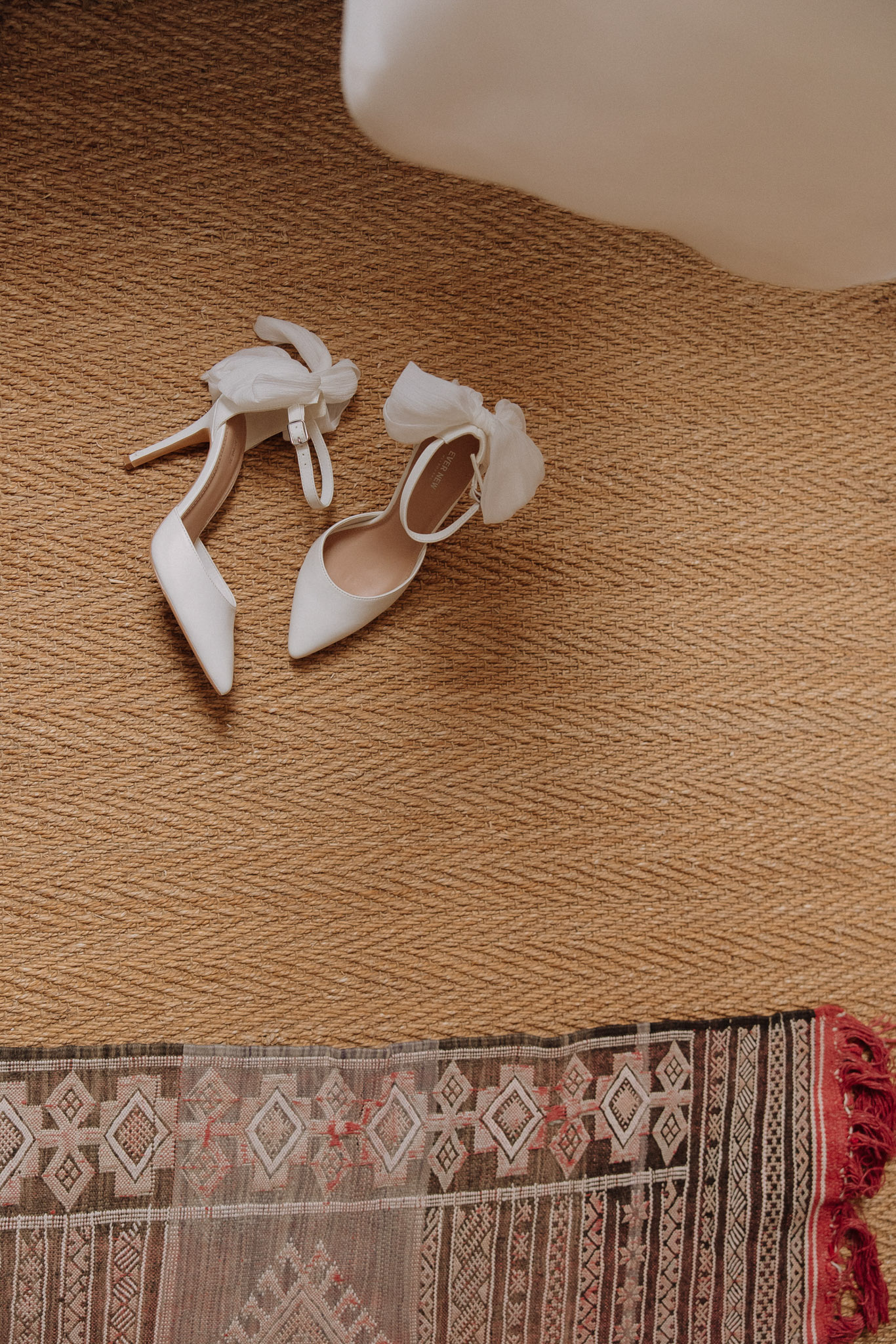 White pointed-toe stilettos with tulle bow embellishments on jute rug with geometric pattern