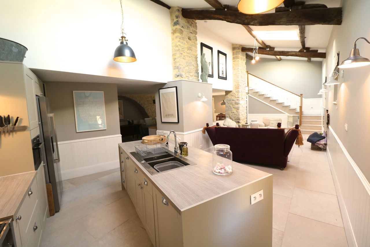 Open-plan kitchen and living area with exposed beams stone columns and contemporary taupe cabinetry in French farmhouse
