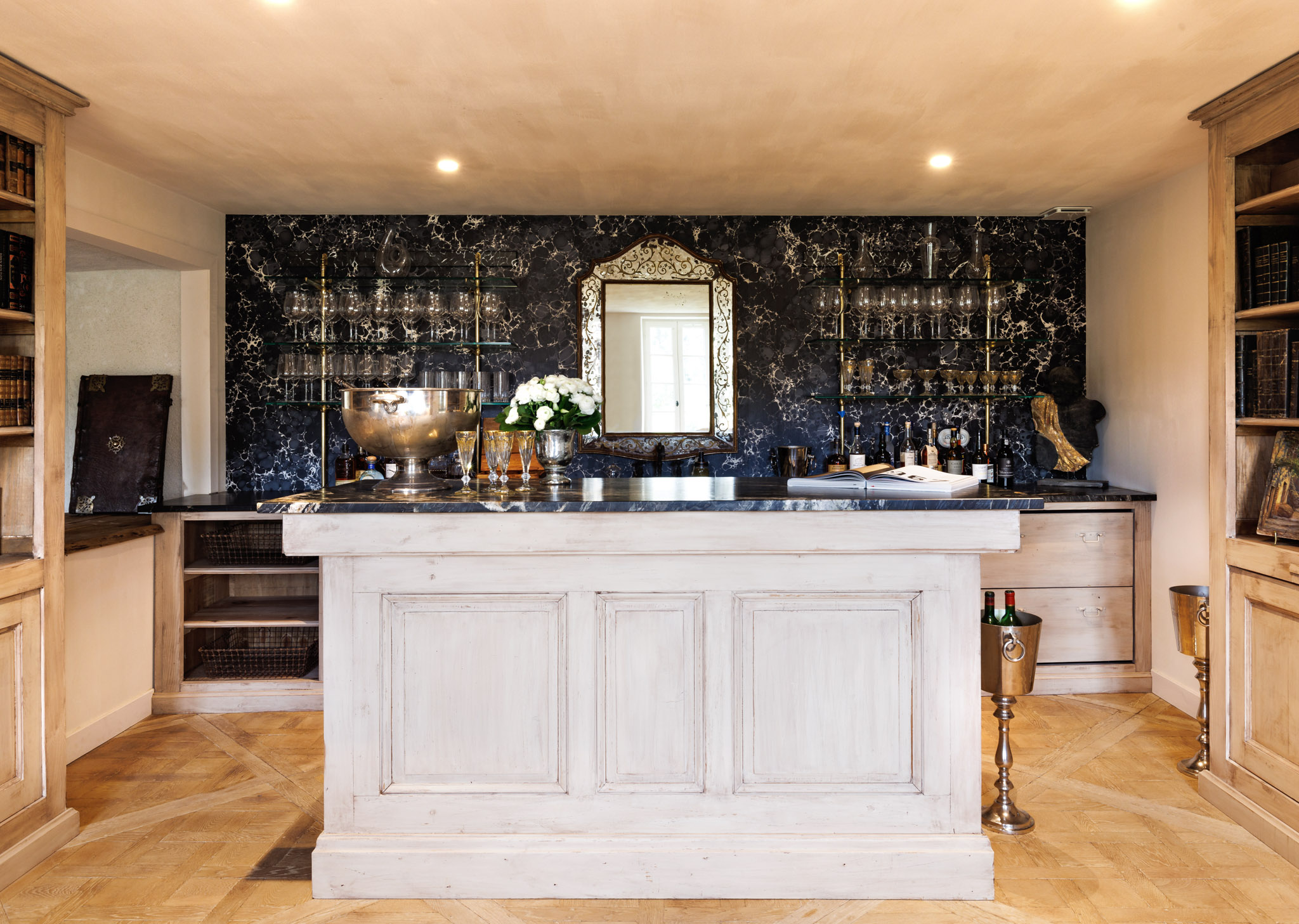 Chateau bar with black marble wall, gilt mirror, silver champagne bowl, white roses, and antique bookshelves