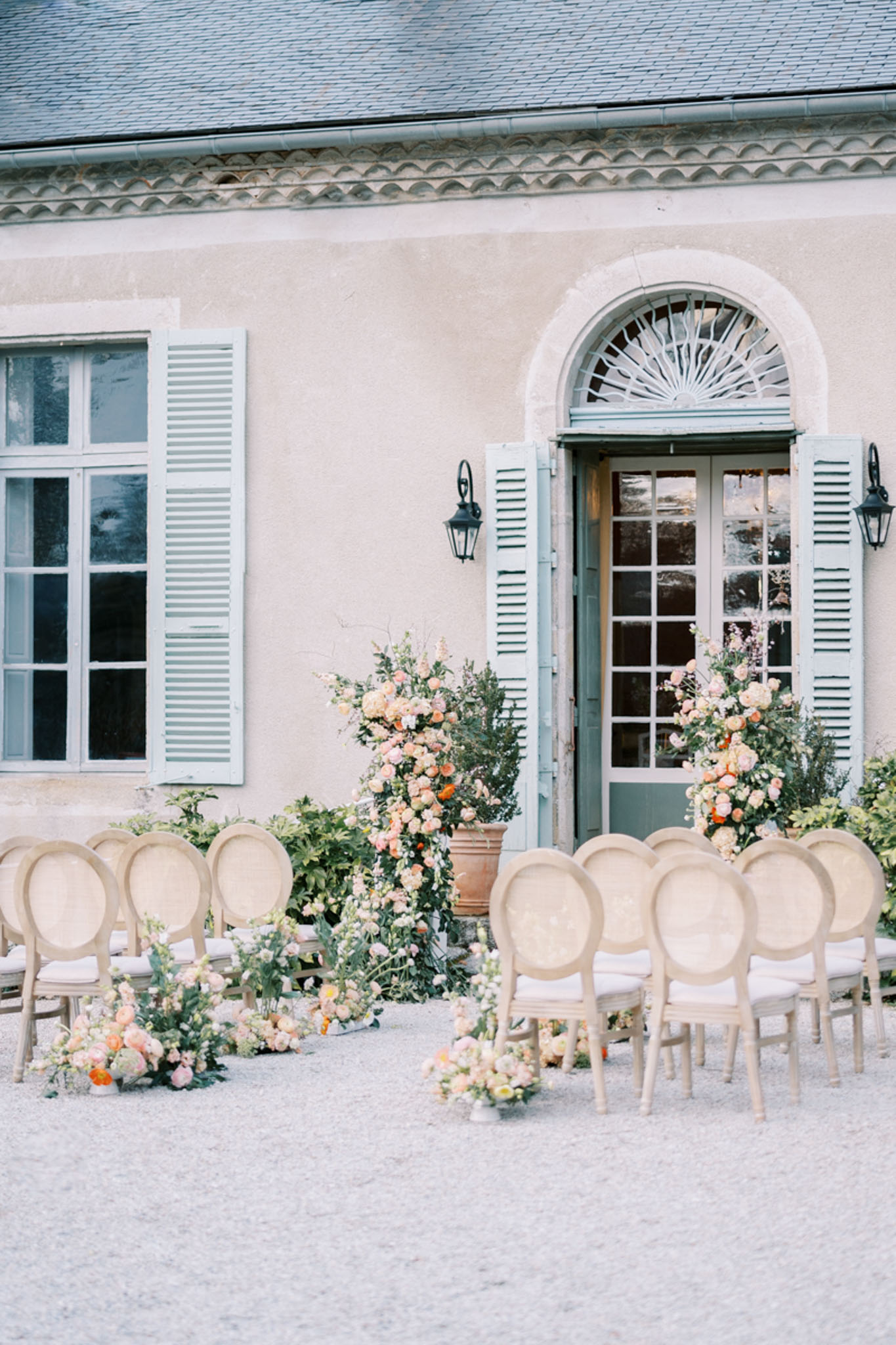 Outdoor ceremony setup at French chateau with cane-back chairs and peach floral arrangements in terracotta urns