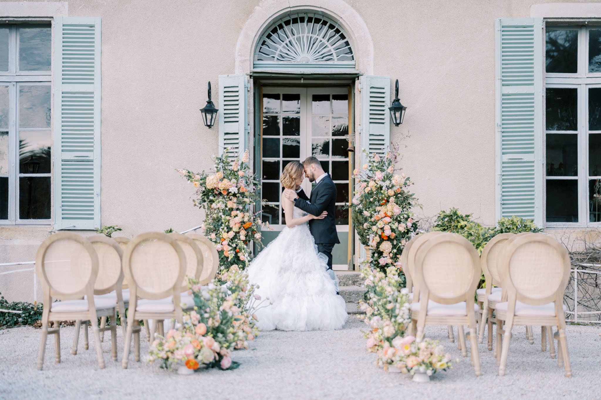 Bride and groom at altar before blush-pink bastide with peach rose floral column arrangements