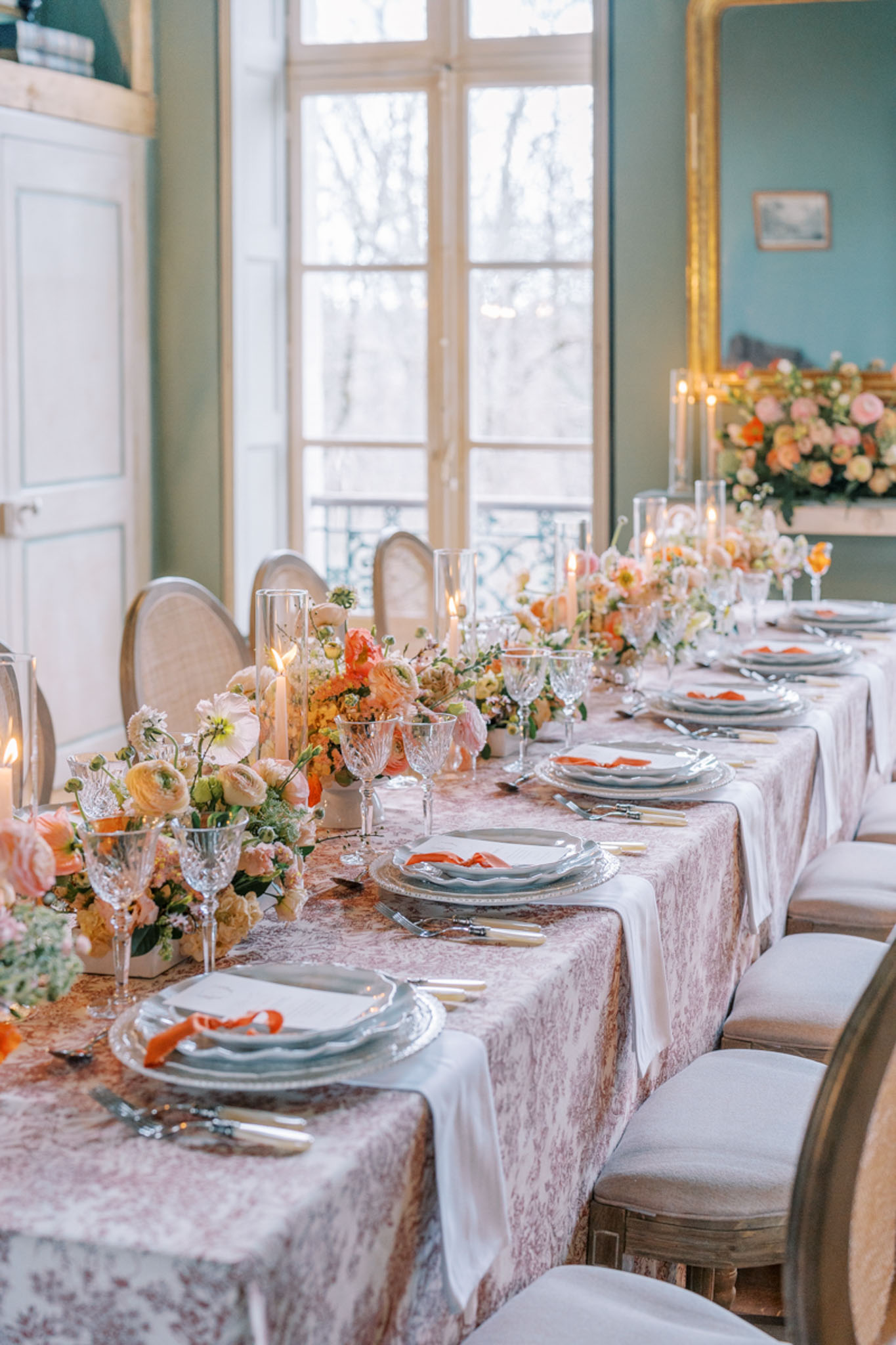 Reception table with peach ranunculus, coral roses, orange ribbon accents, and sage green walls