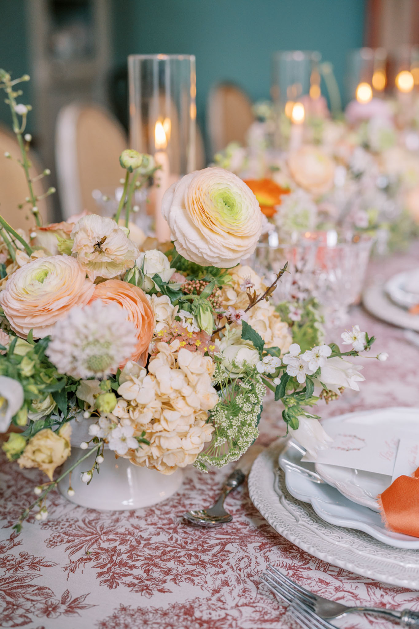 Reception place setting with peach ranunculus centerpiece on dusty rose toile tablecloth and scallop charger plates