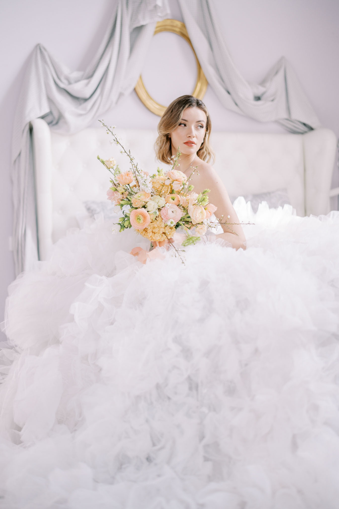 Bride in ruffled tulle ball gown with peach ranunculus and yellow carnation bouquet in white studio interior