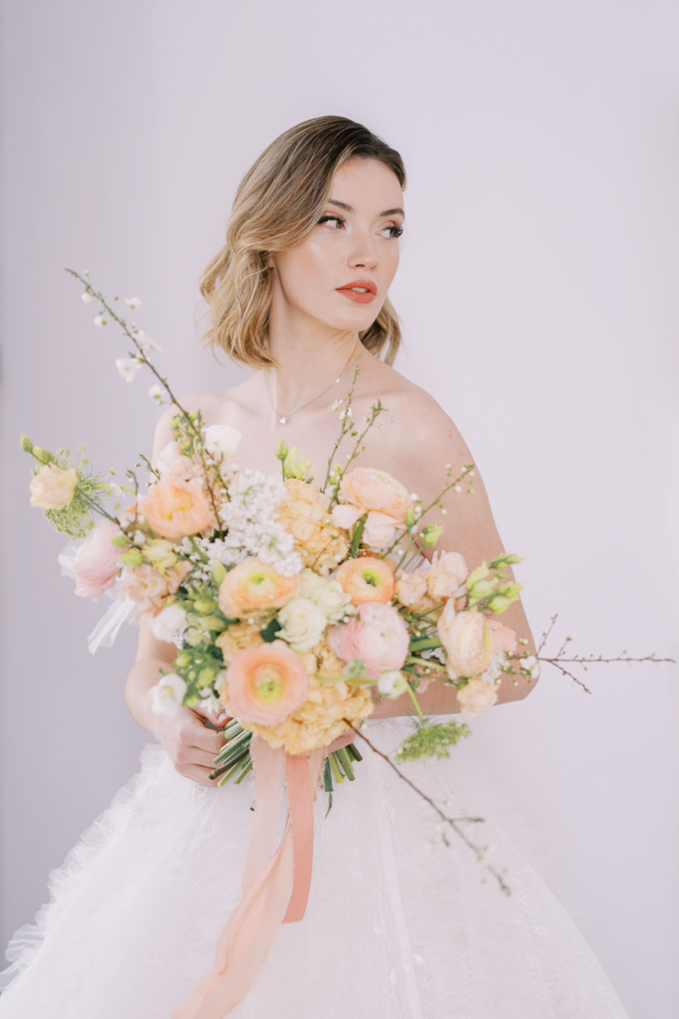 Bride in strapless white tulle ballgown holding a peach and coral ranunculus bouquet with trailing ribbon