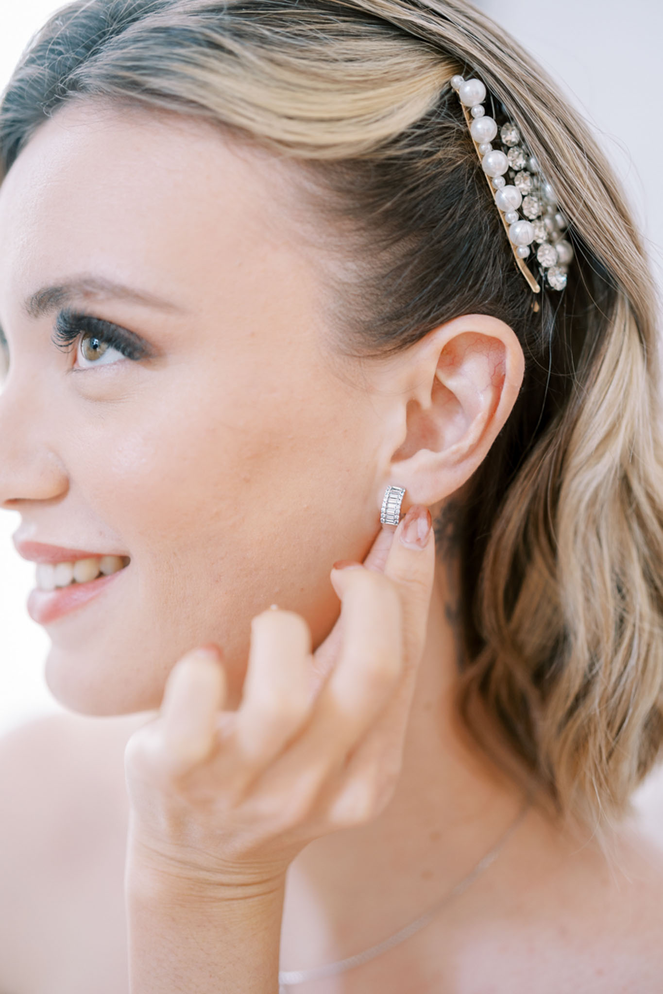 Close-up of bride adjusting diamond baguette hoop earring with pearl and crystal hair comb
