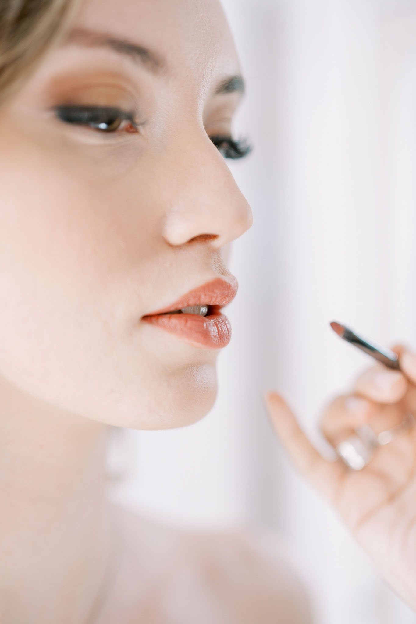 Makeup artist applying terracotta lip liner to bride during getting ready preparations