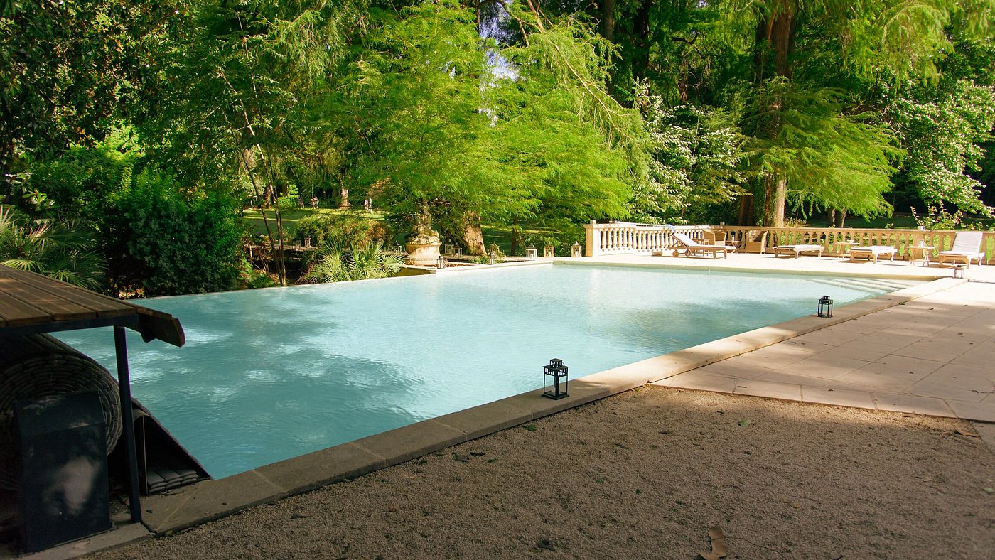 Rectangular swimming pool with stone balustrade wooden sun loungers and estate grounds