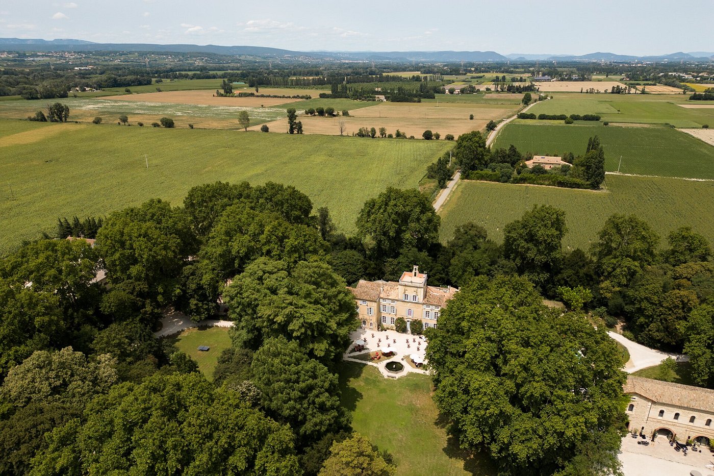 Aerial view of stone chateau with fountain courtyard barn and vineyard fields to horizon