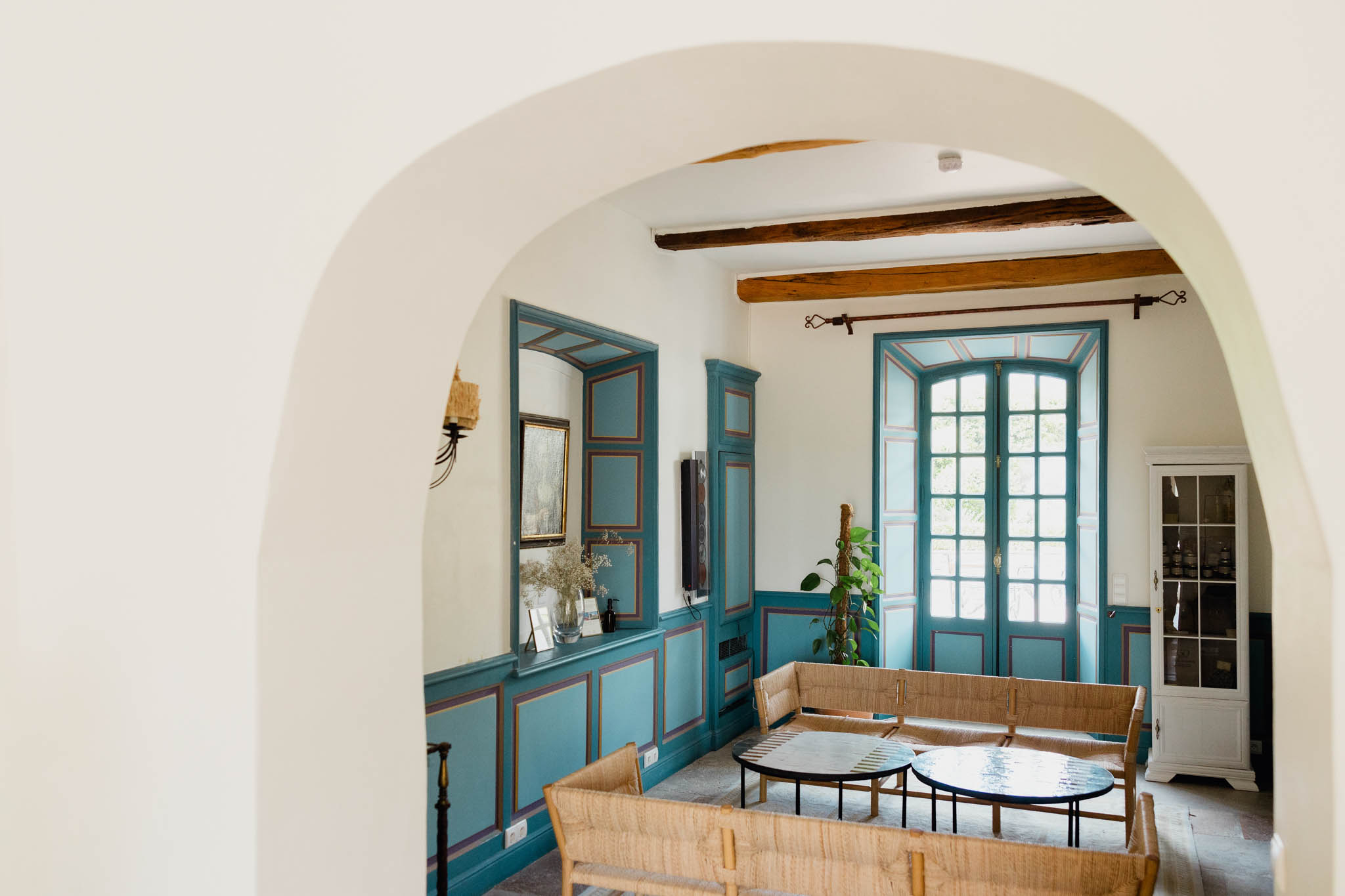 Teal-panelled salon with rattan furniture viewed through rounded archway in French chateau interior