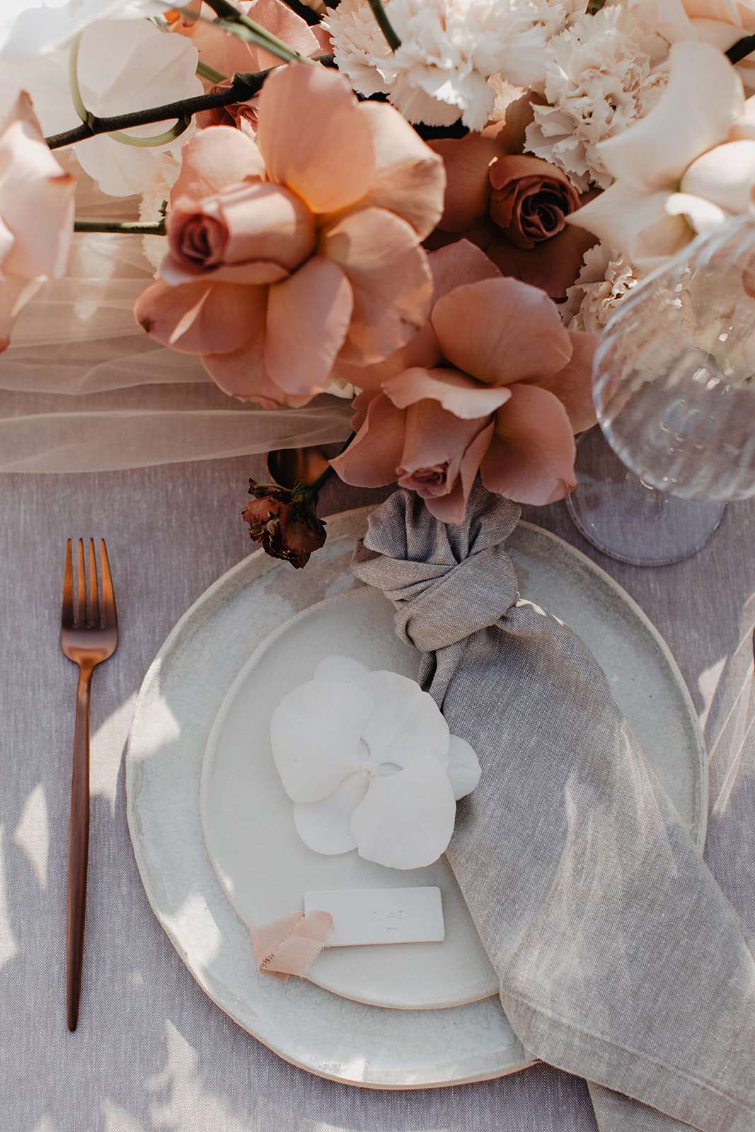Grey-blue plate with knotted linen napkin and blush rose and orchid centrepiece on grey tablecloth