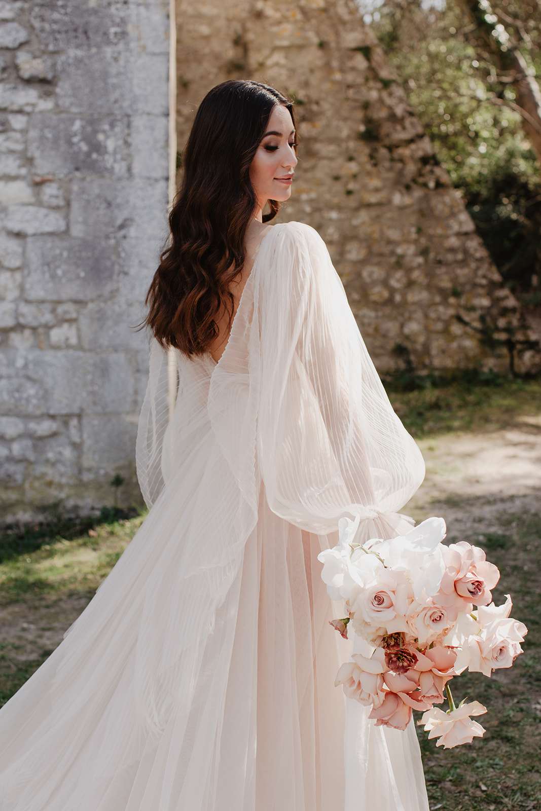 Bride in blush pink tulle ball gown holding a trailing bouquet of roses photographed from behind