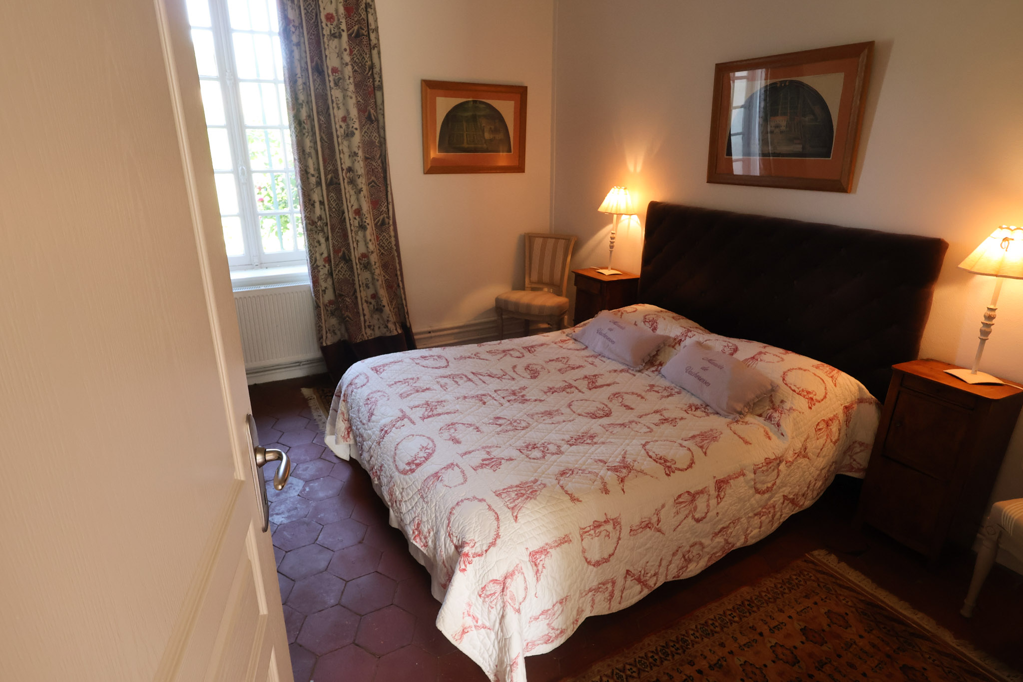 Guest bedroom in French manor with toile bedding, terracotta tile floors, and floral curtains