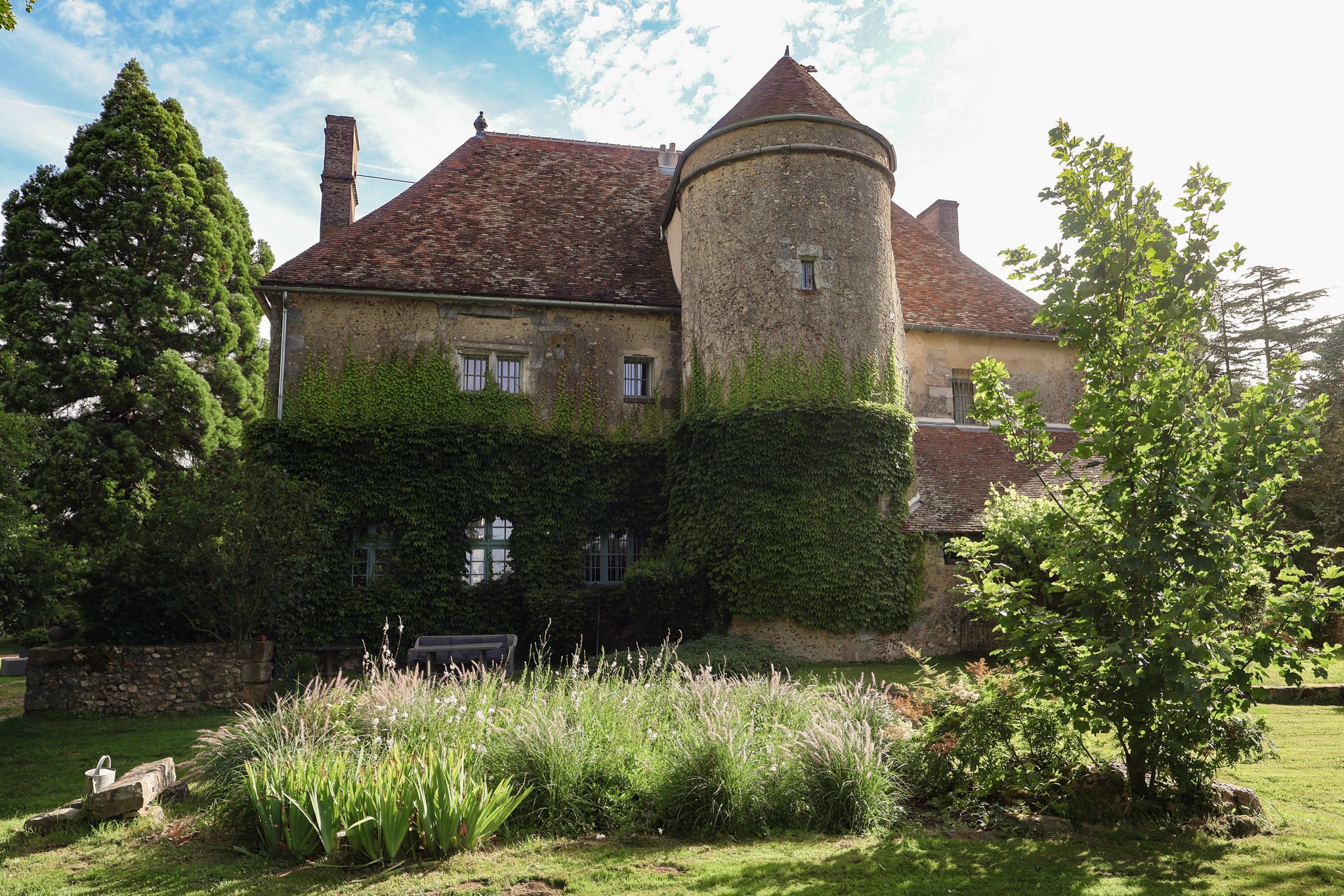 French chateau exterior with ivy-covered facade, round stone tower with terracotta roof, and garden beds