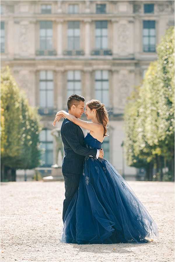 Couple embracing before Parisian classical building bride in navy blue tulle ballgown groom in navy pinstripe suit