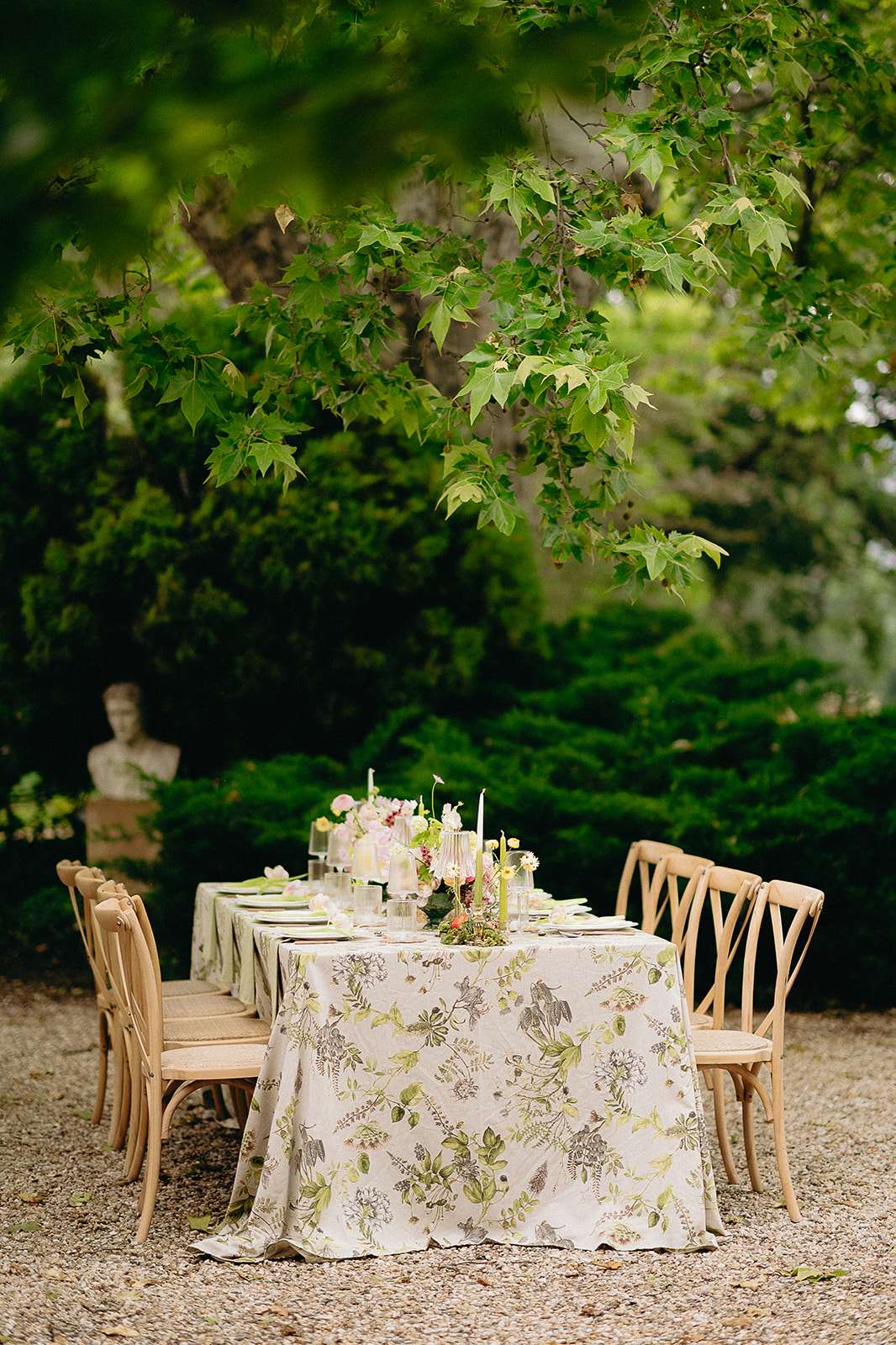 Garden table with botanical-print linen bud vase florals white taper candles and stone bust backdrop