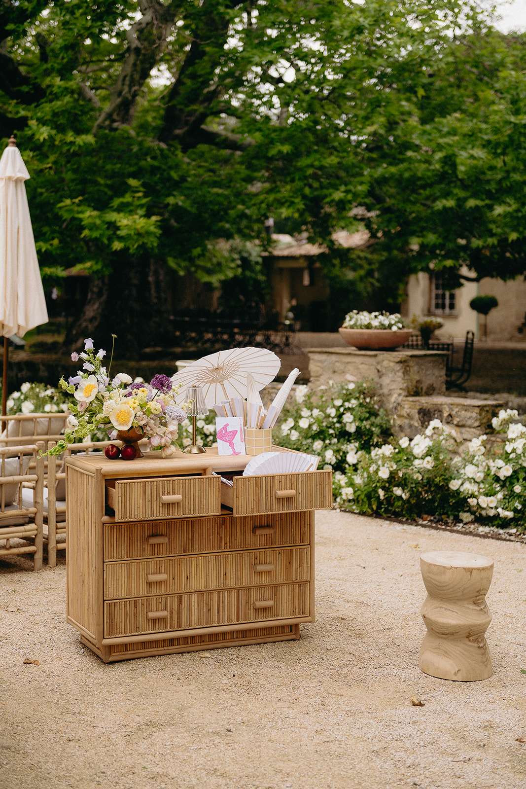 Rattan dresser welcome station with yellow and purple floral arrangement and paper fans at a French estate