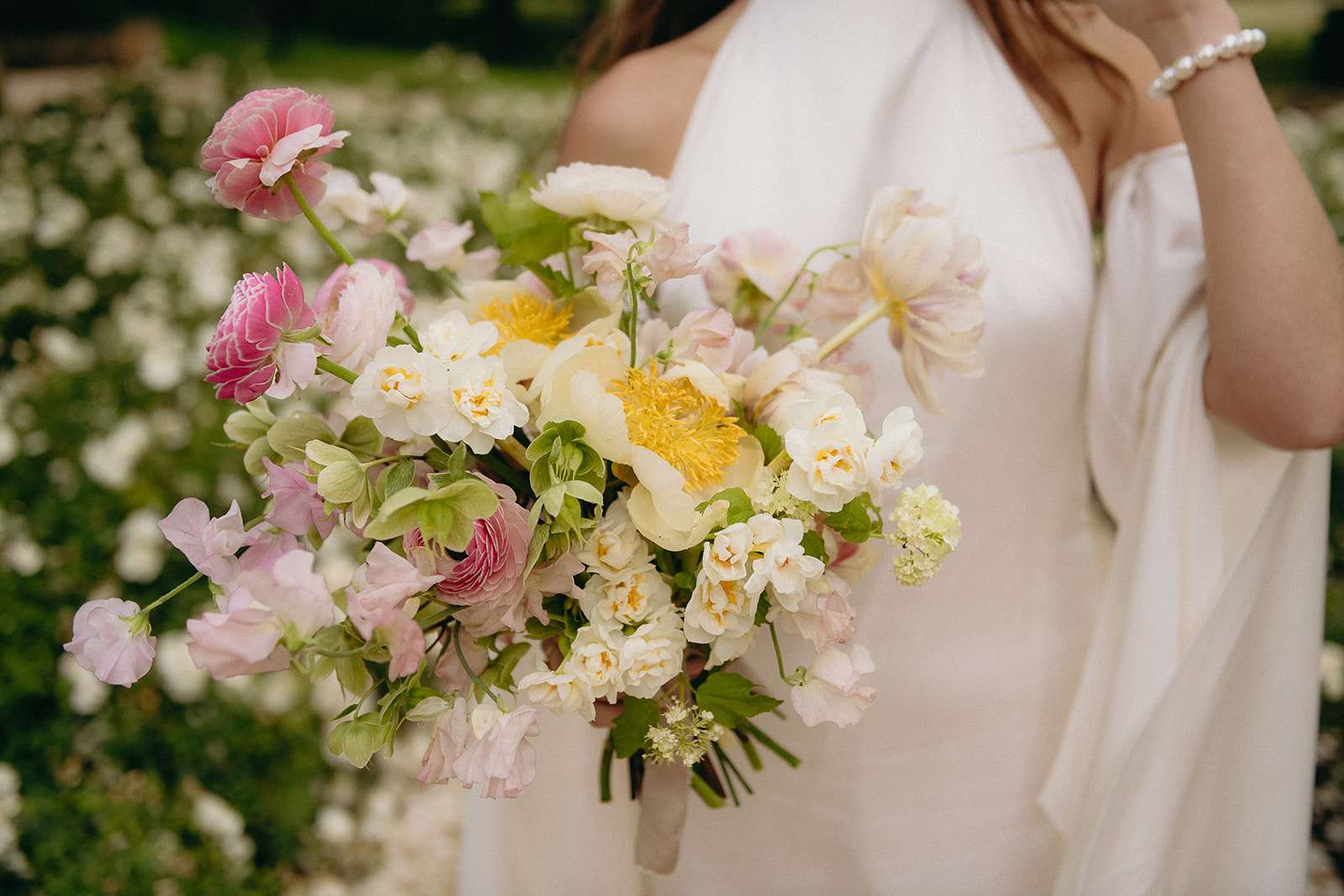 Close-up of bride holding a garden-style bouquet with yellow peonies, pink ranunculus, and sweet peas