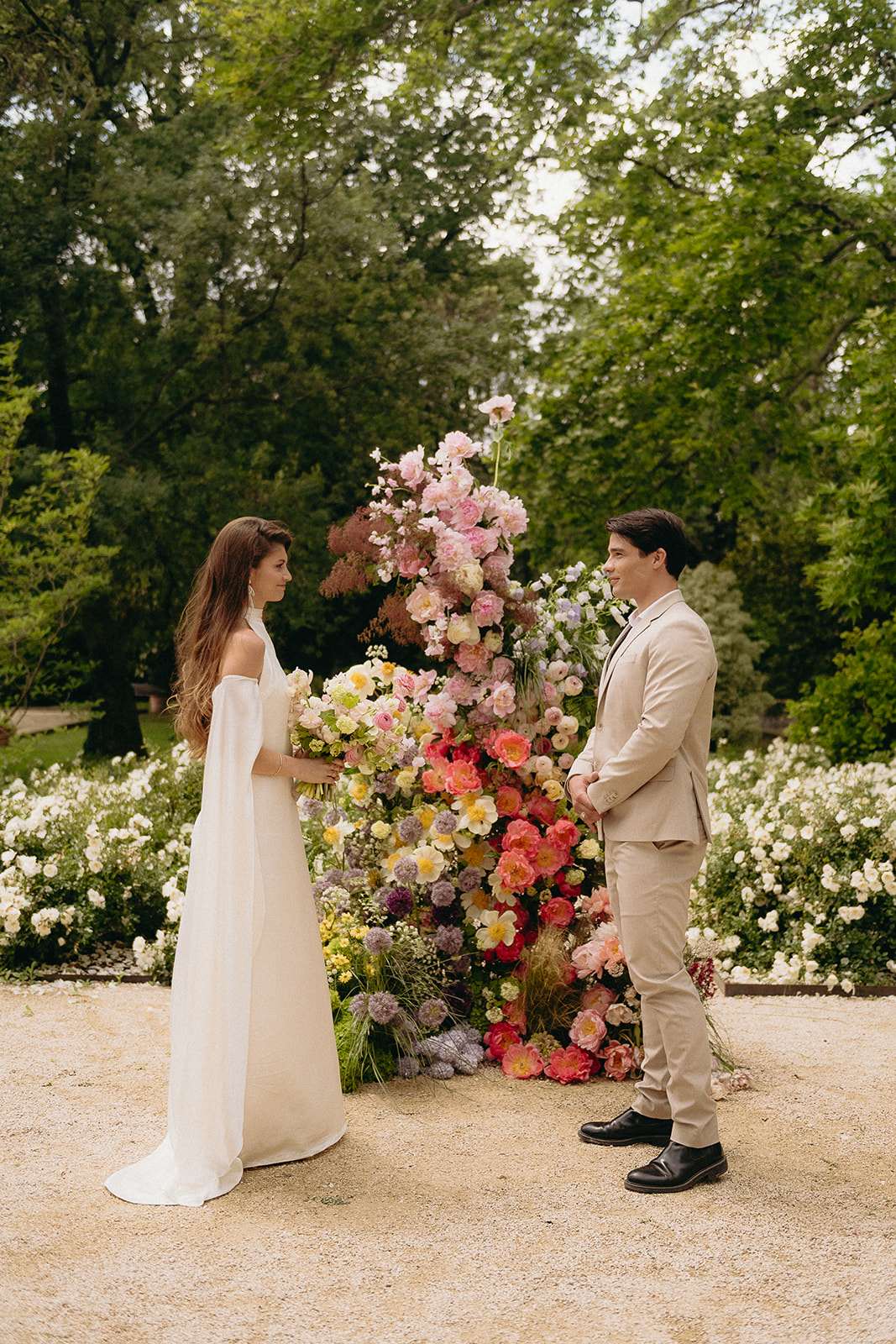 Couple before tall vertical floral column of pink peonies, coral ranunculus, and purple allium