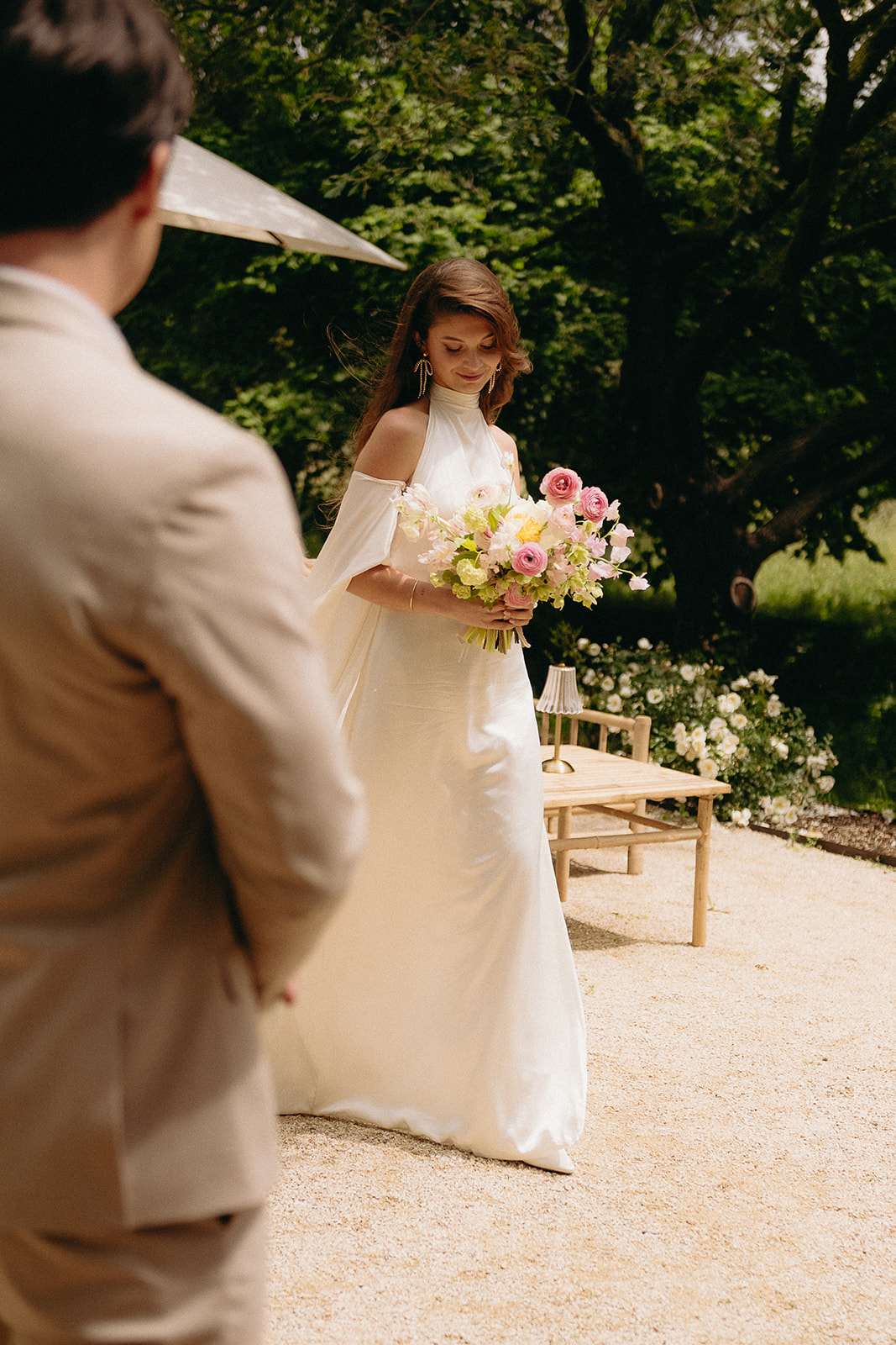 Bride walking toward groom during first look holding pink ranunculus and yellow bloom bouquet