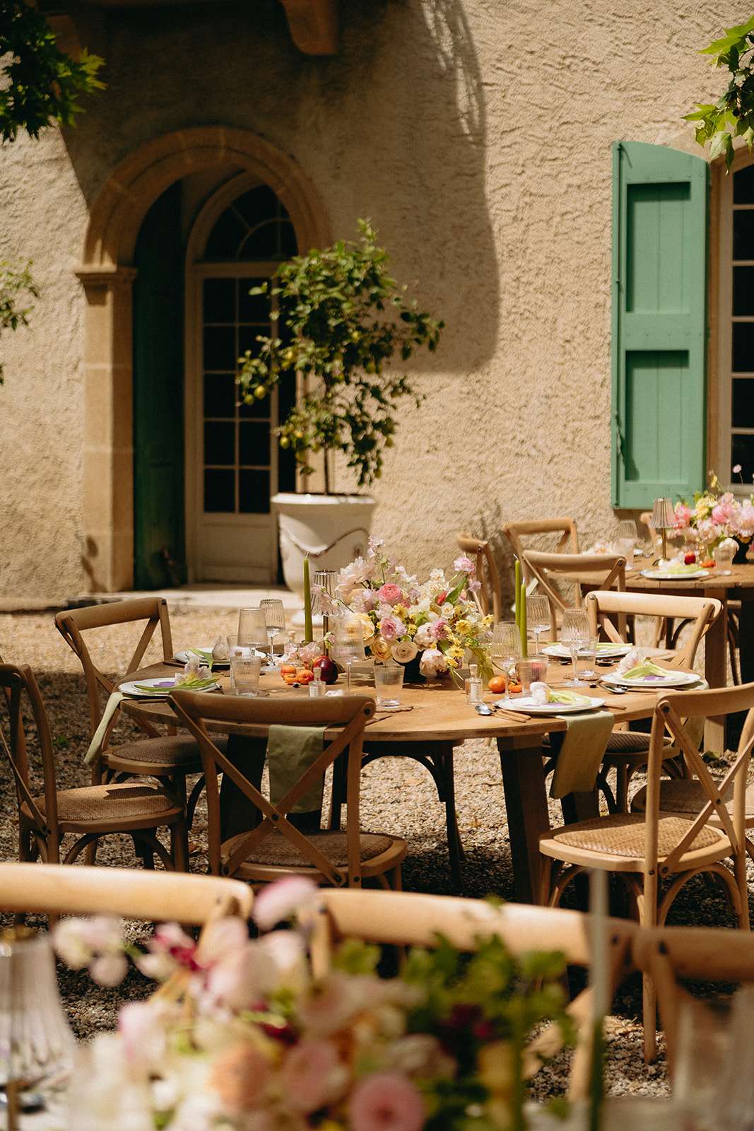 Bastide courtyard reception round tables with sage runner pink ranunculus cream peonies green tapers and scattered fruit