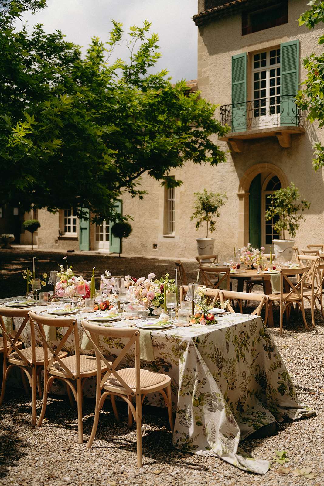 Long head table with botanical-print linen, blush peony centrepieces, and green tapers before stone manor