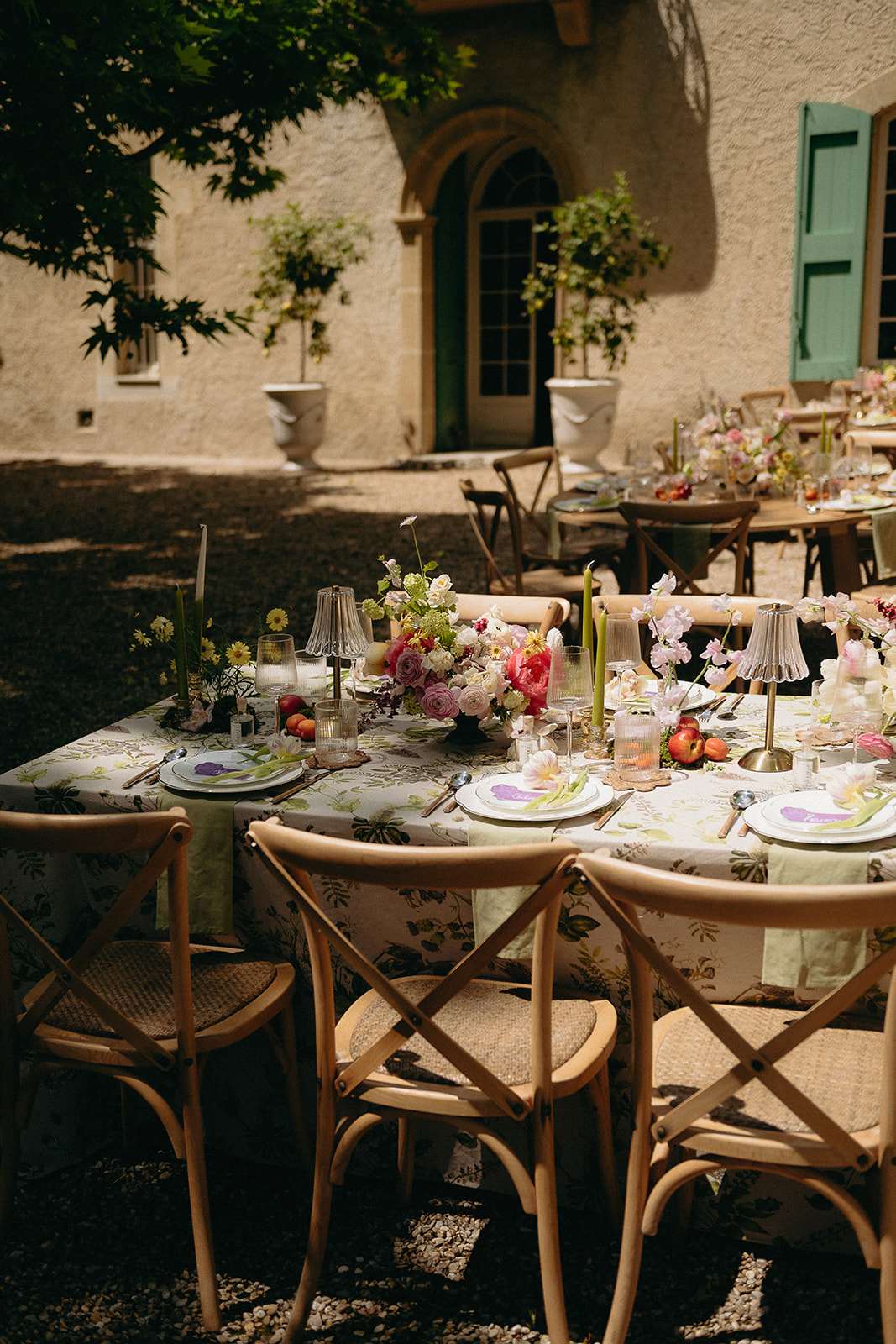 Garden table with botanical linen hot pink ranunculus green taper candles cross-back chairs and fresh peaches