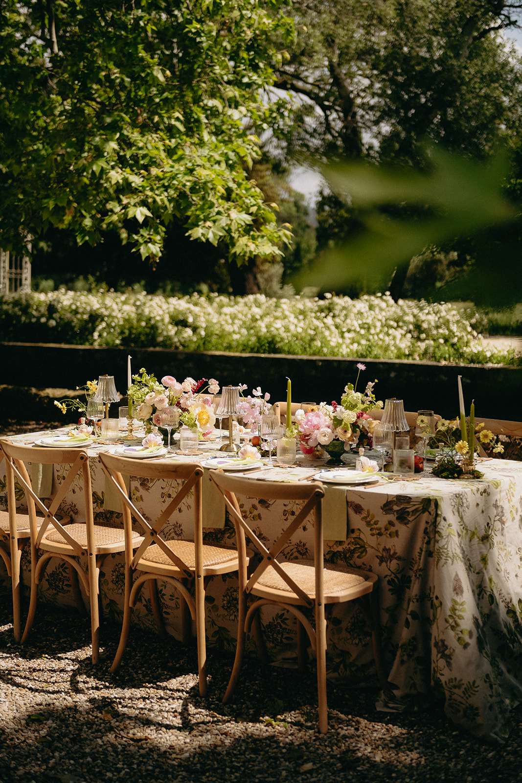 Garden reception table with botanical-print linen, pink ranunculus, yellow poppies, and olive taper candles