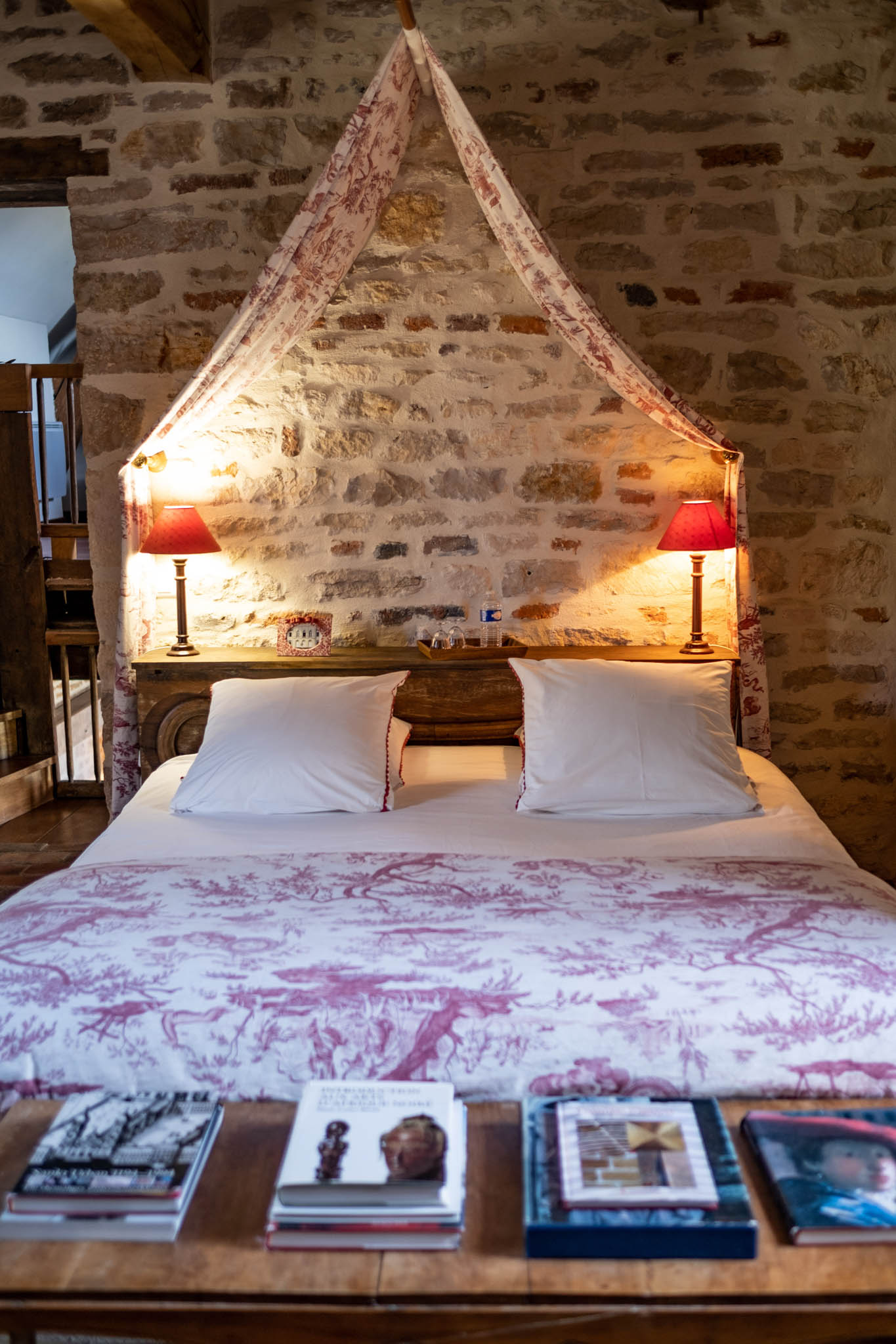 Guest bedroom in historic French stone building with red and white toile de Jouy canopy and exposed stone walls