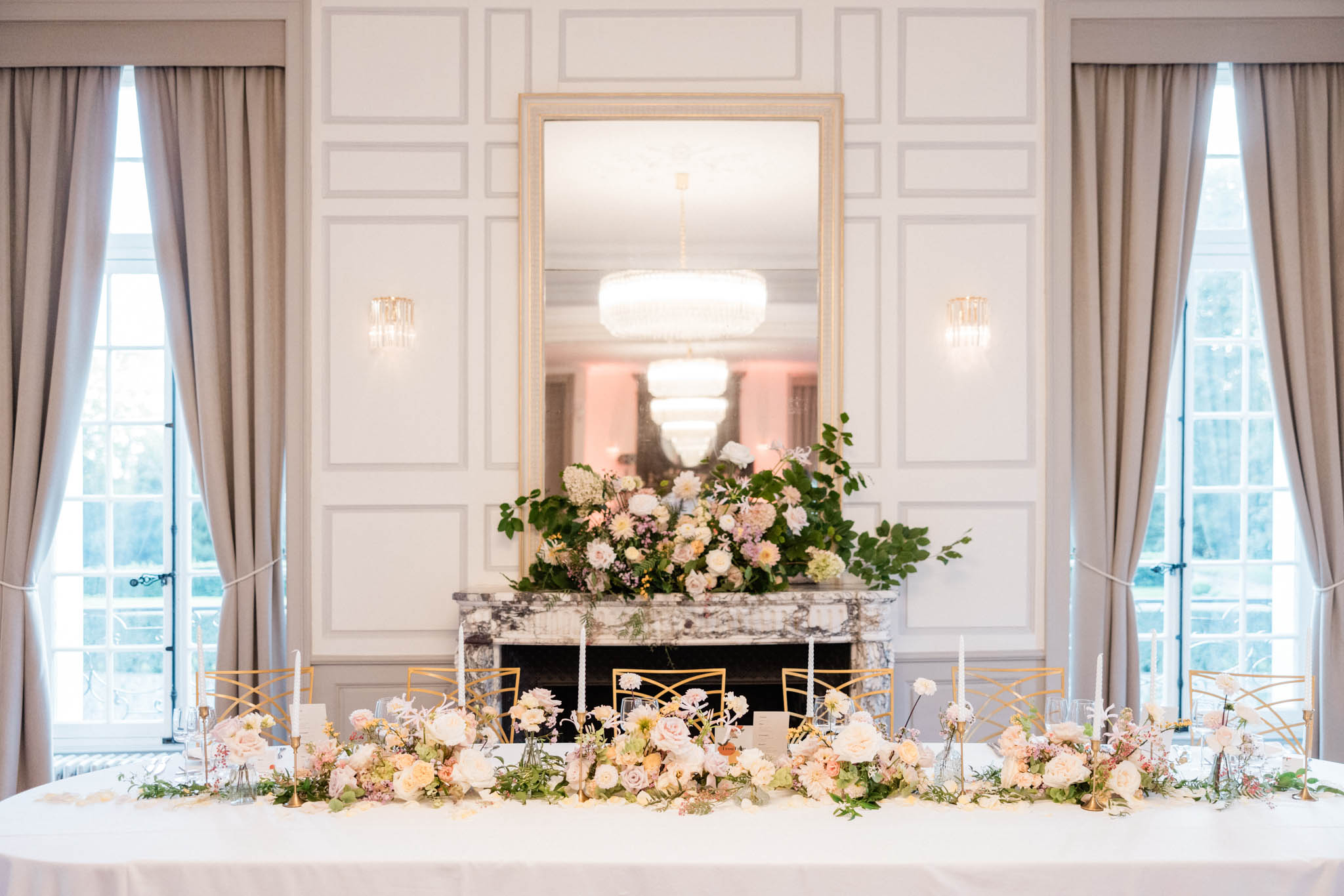 Wedding head table with blush and cream floral runner, gold candlesticks, and marble fireplace in a chateau salon